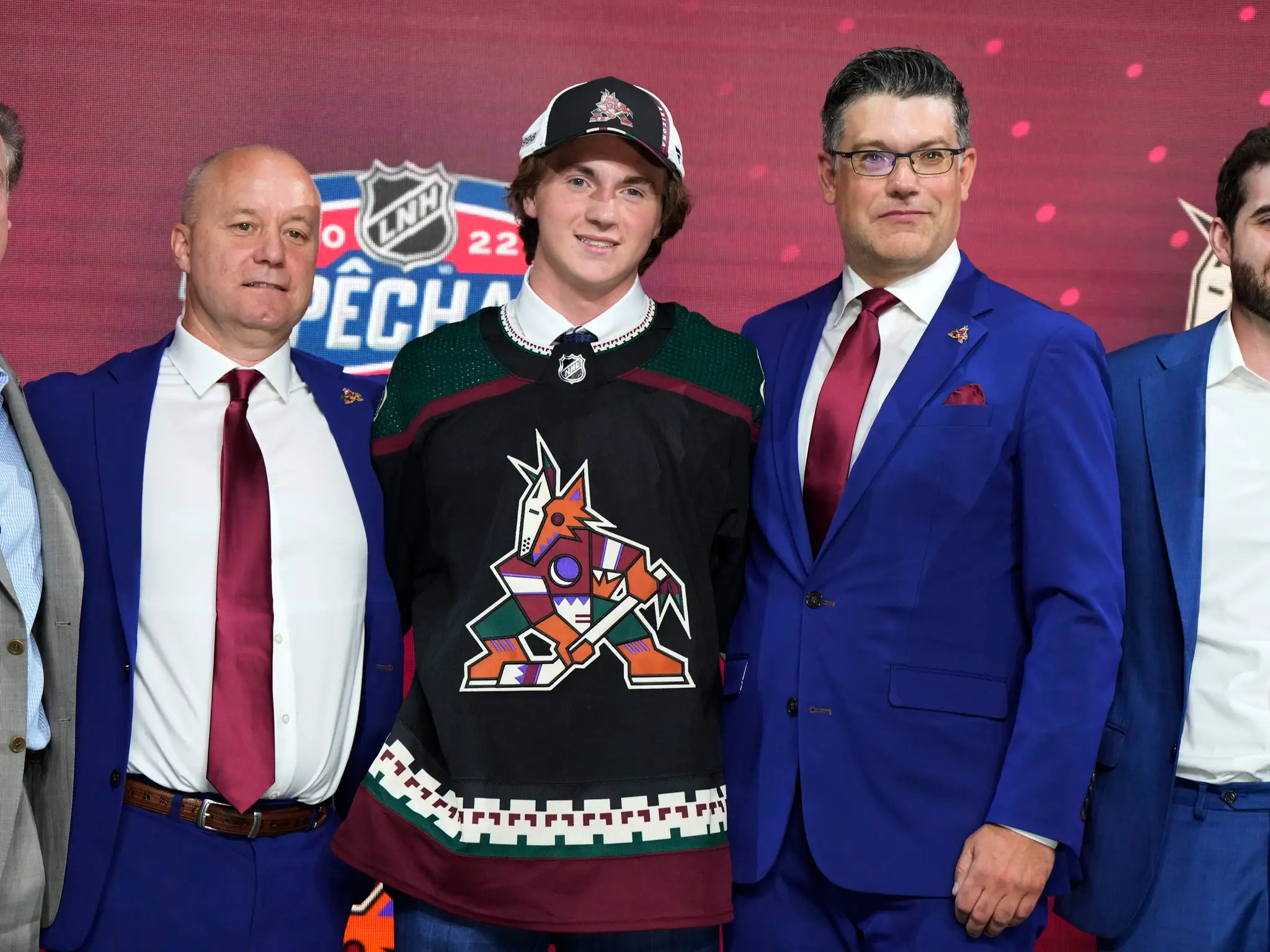 Logan Cooley ako trojka draftu pózuje v drese Arizony s predstaviteľmi klubu.
