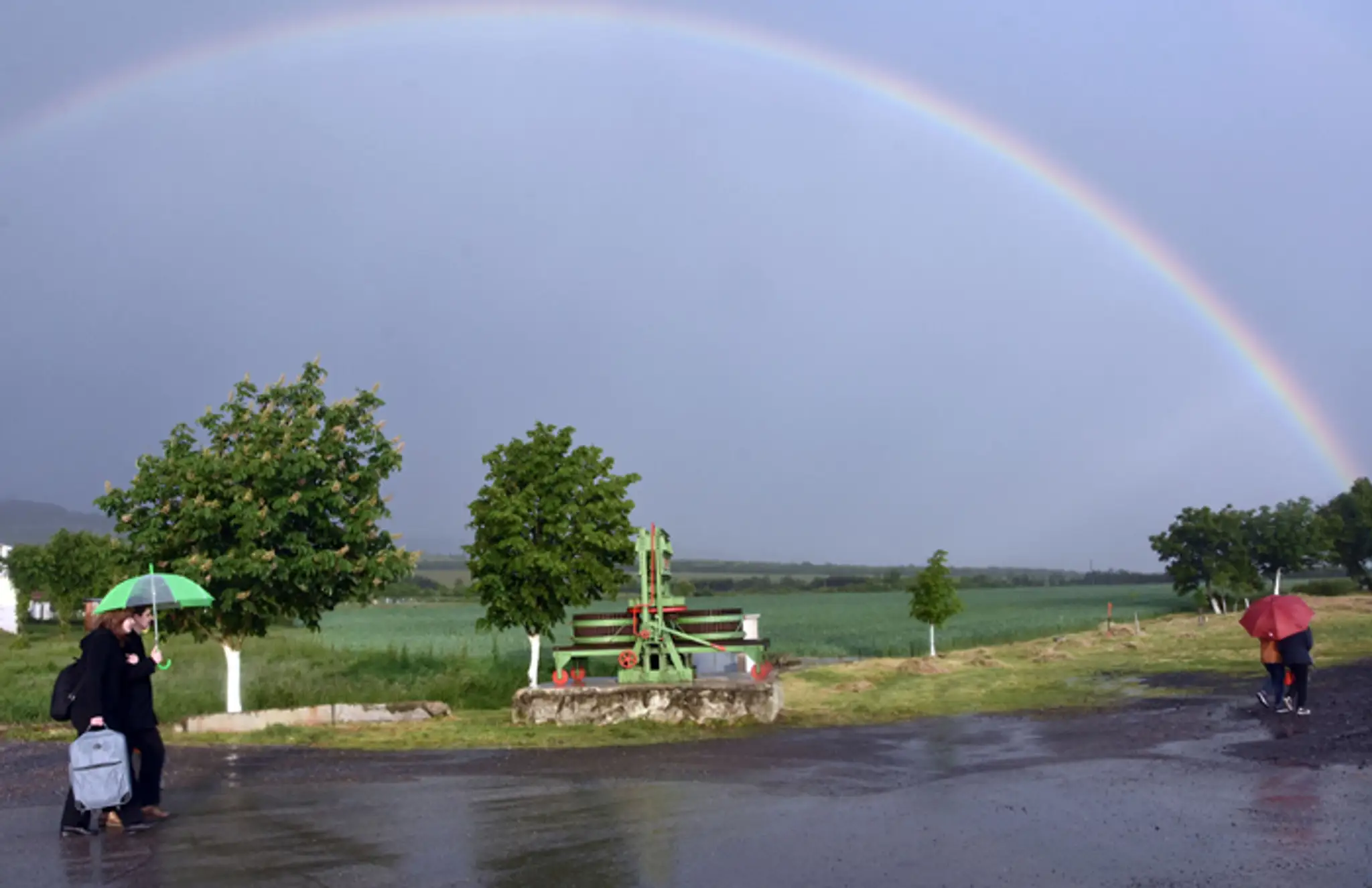 Ľudia v daždi prechádzajú pred dúhov v obci Čerhov.