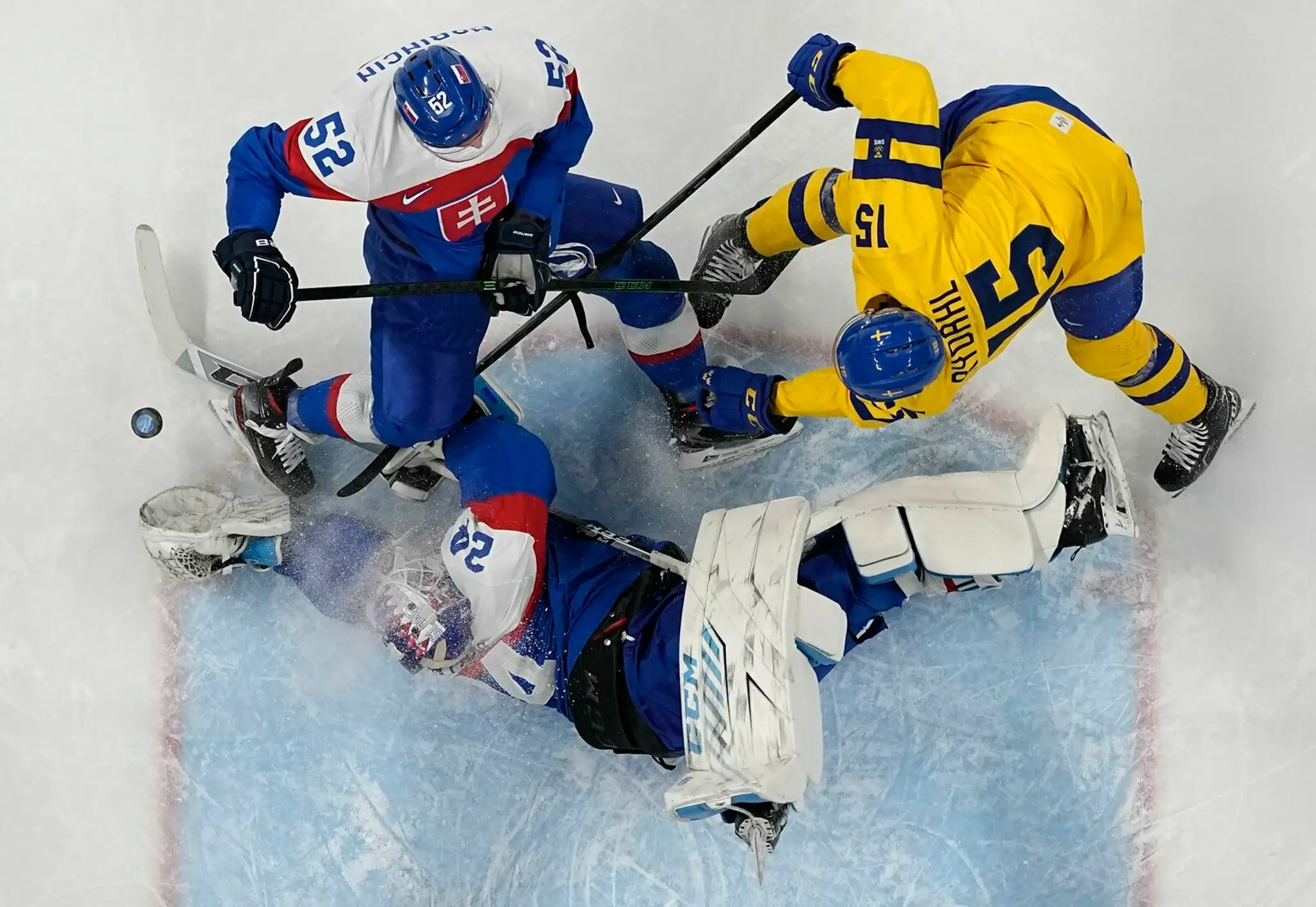 Gólman Slovenska Patrik Rybár sa snaží chytiť puk pred Švédom Gustavom Rydahlom a našim Martinom Marinčinom v dueli ZOH 2022.