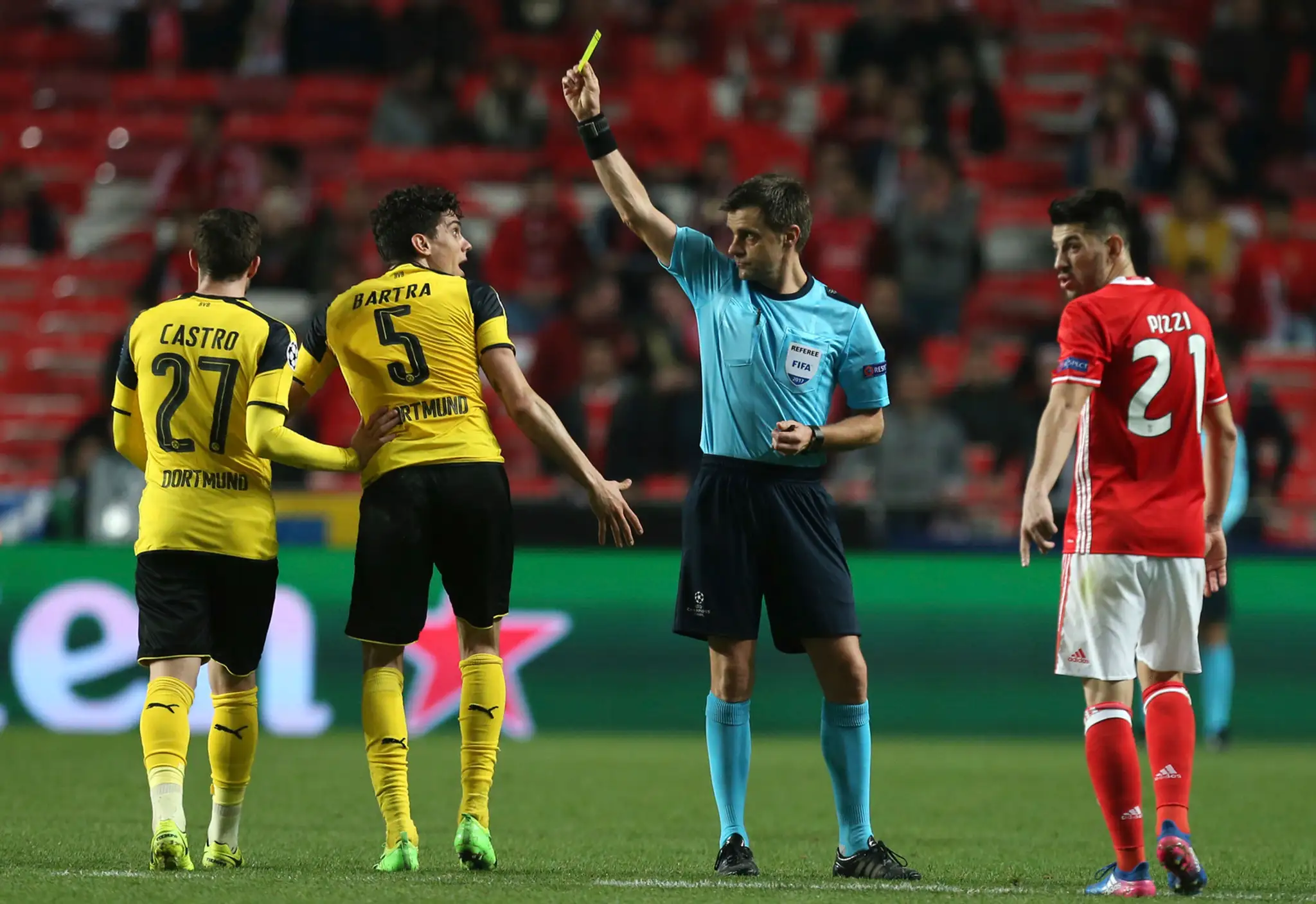 Arbiter Nicola Rizzoli ukazuje žltú kartu Marcovi Bartrovi z Dortmundu (číslo 5) v osemfinále LM proti Benfice.