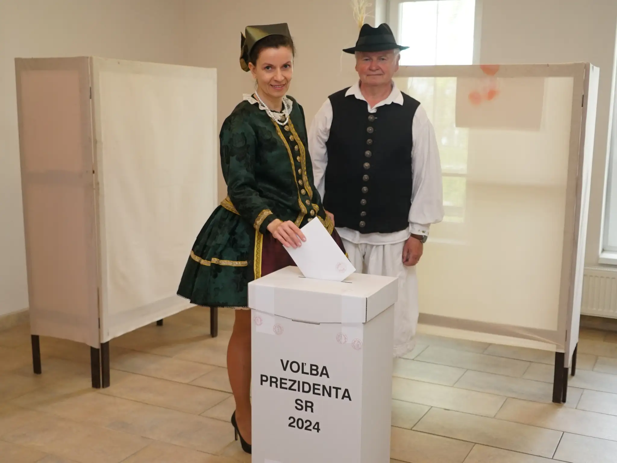 Členovia súboru ľudových tradícií Gyöngyösbokréta odetí v kroji vhadzujú obálky s hlasovacím lístkom v obci Iža v okrese Komárno.