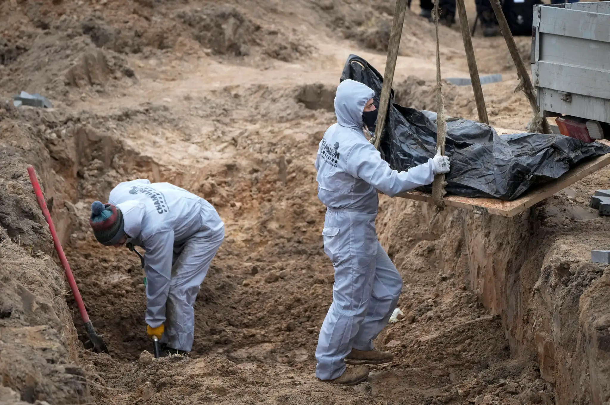 Muži v ochranných odevoch exhumujú telá civilistov v ukrajinskom meste Buča.