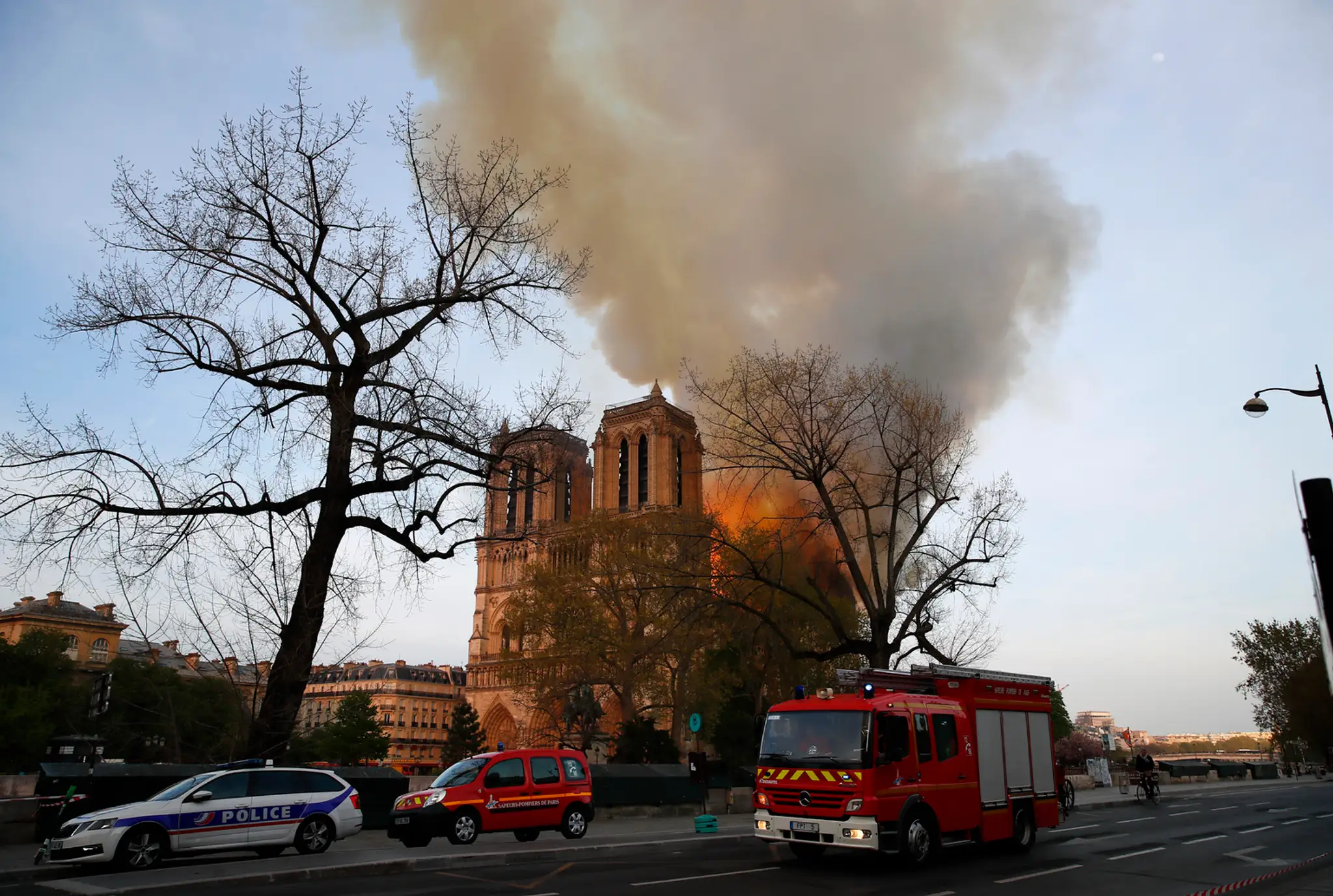 Ľudia, stojac pri rieke Seina, sledujú požiar katedrály Notre Dame.