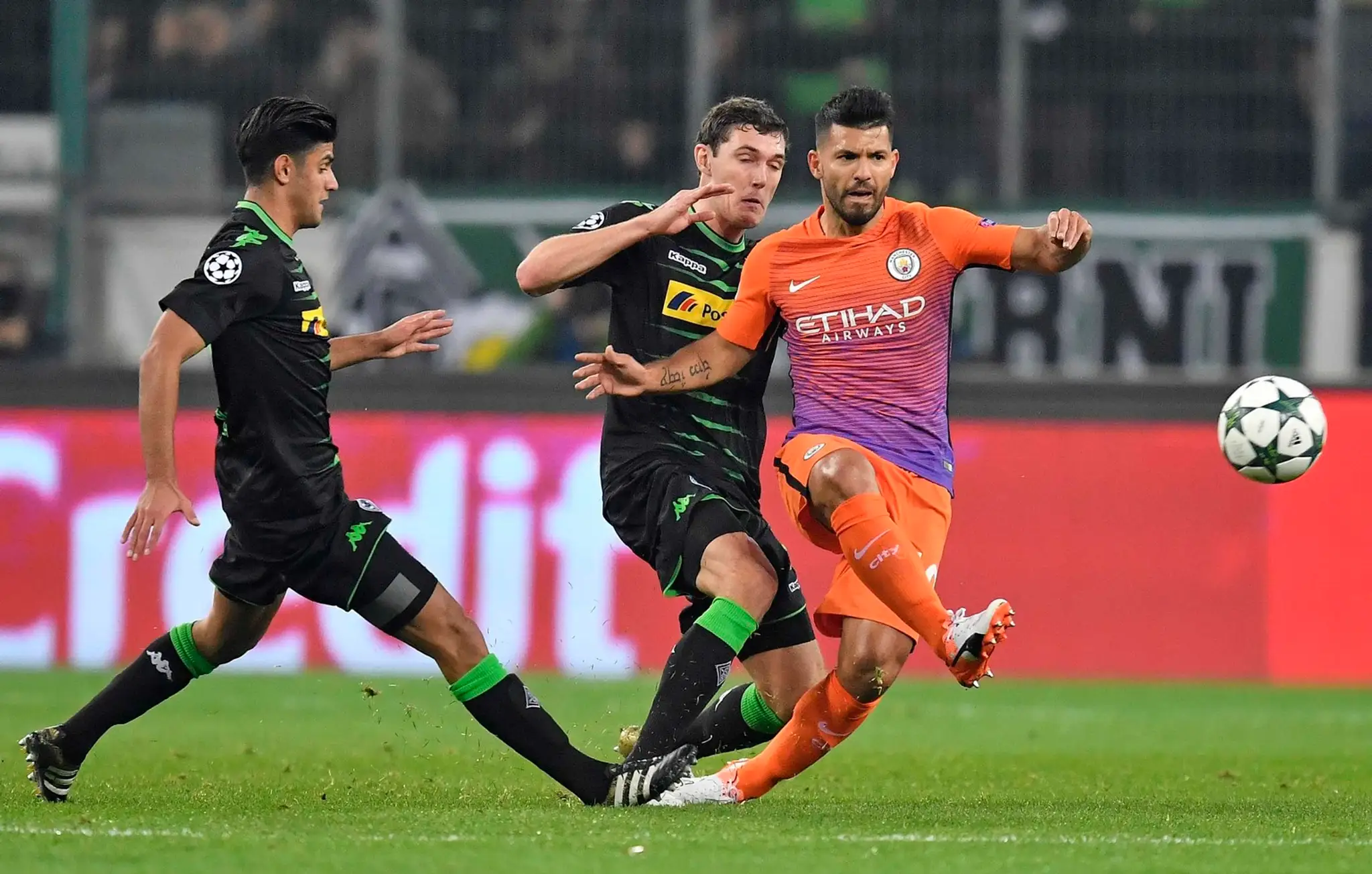 Kanonier Manchestru City Sergio Agüero odkopáva loptu pred dvojicou hráčov Borussie Mönchengladbach v dueli LM.