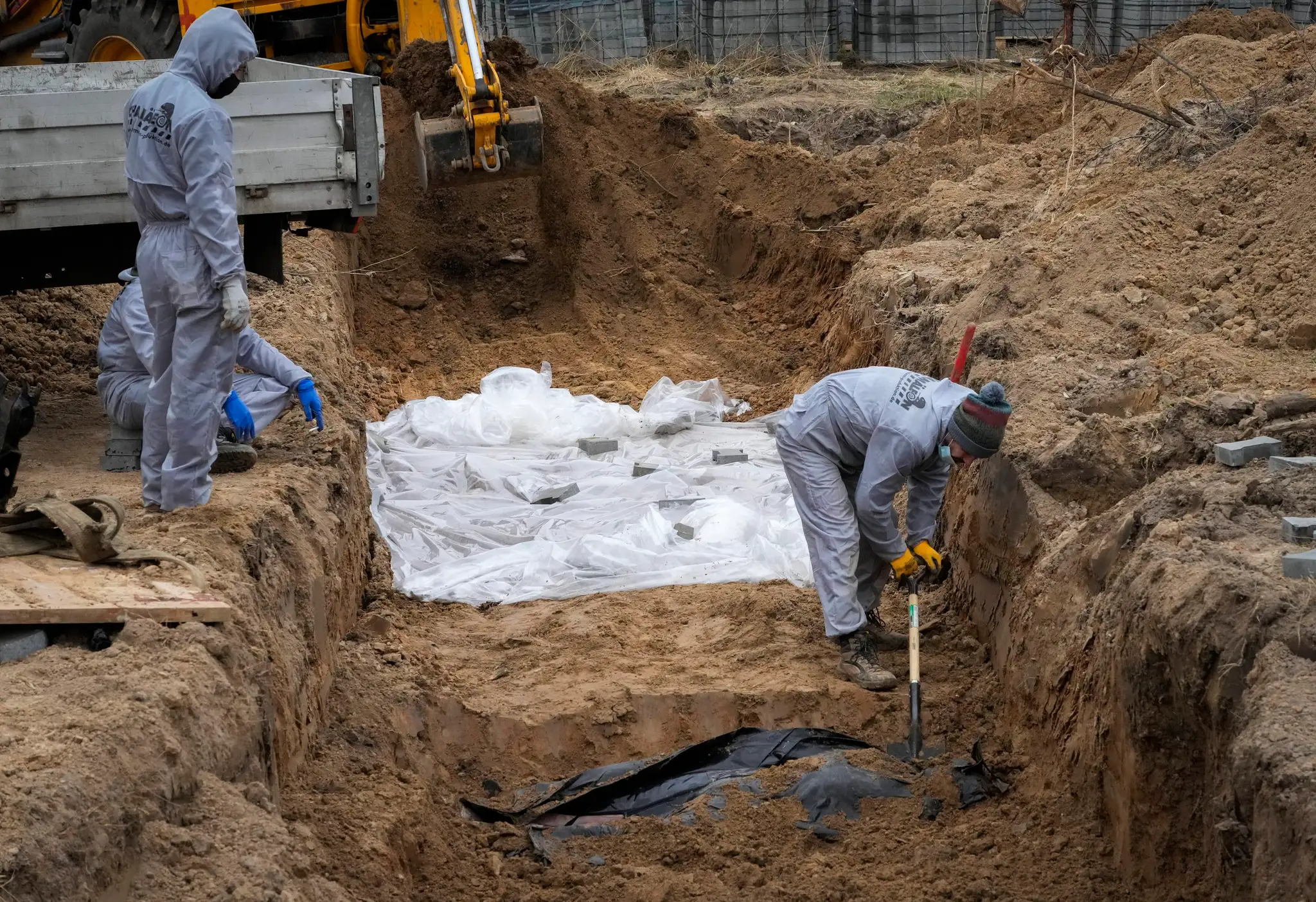 Muži v ochranných odevoch exhumujú telá civilistov v ukrajinskom meste Buča.