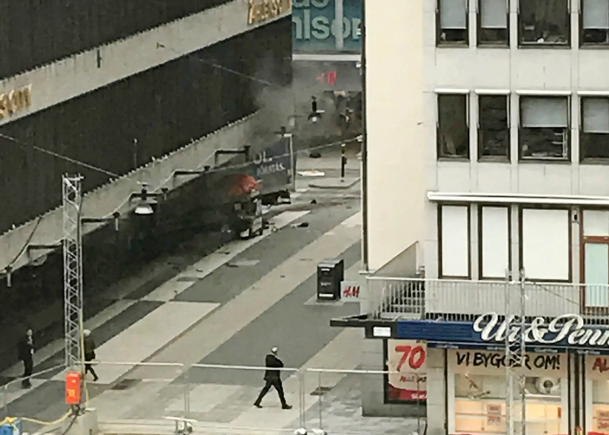 Okoloidúci sa pozerajú na nákladné auto, ktoré vrazilo do obchodného domu na pešej zóne v centre Štokholmu.