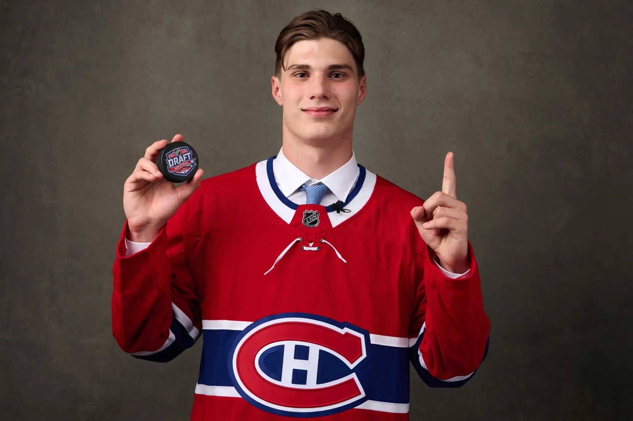 Juraj Slafkovský pózuje s pukom v drese Montrealu, ktoré si ho vybralo ako jednotku v drafte NHL 2022.