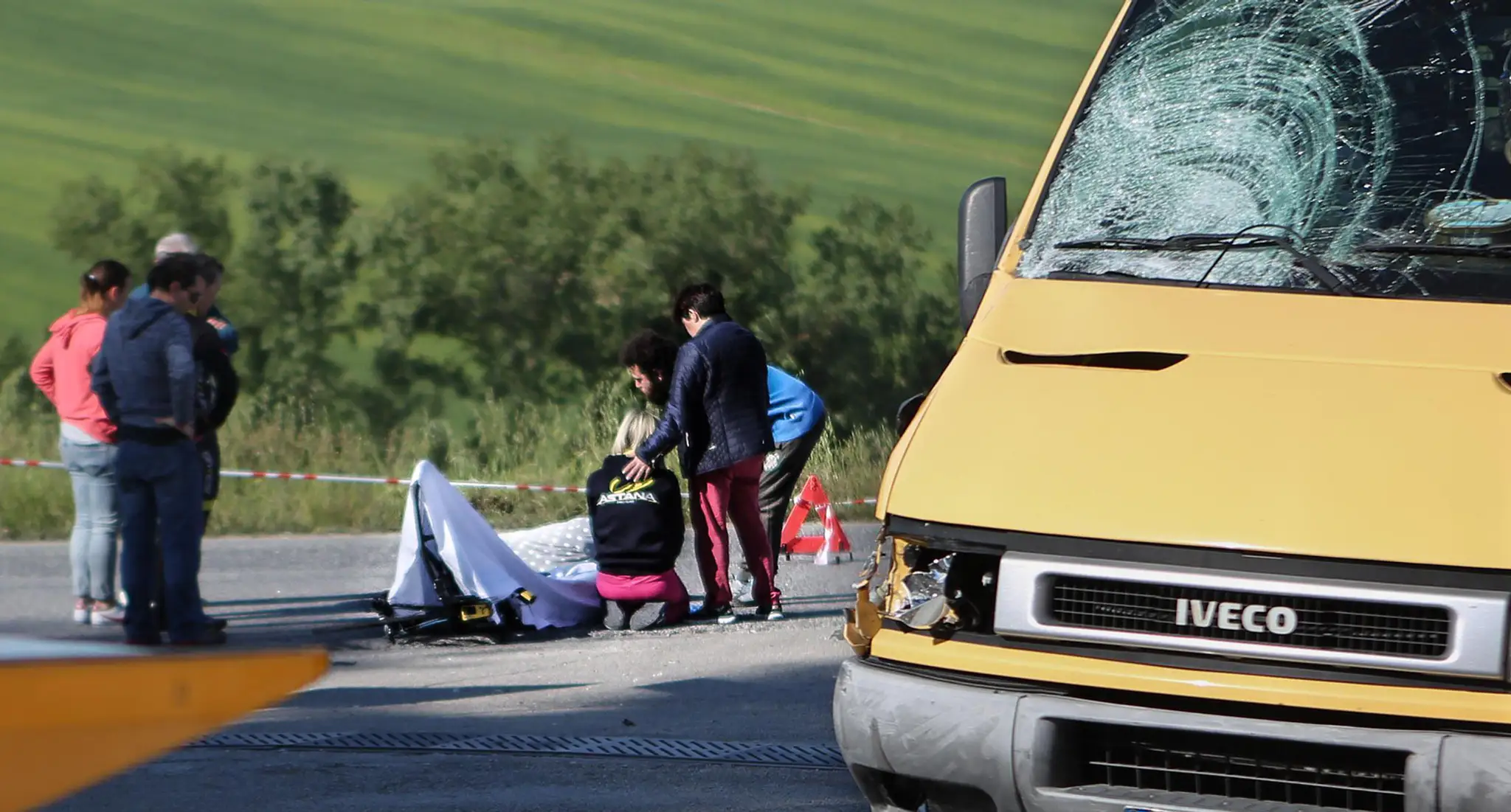 Členka cyklistického tímu Astana kľačí na kolenách vedľa zakrytého bicykla talianskeho cyklistu Michela Scarponiho.