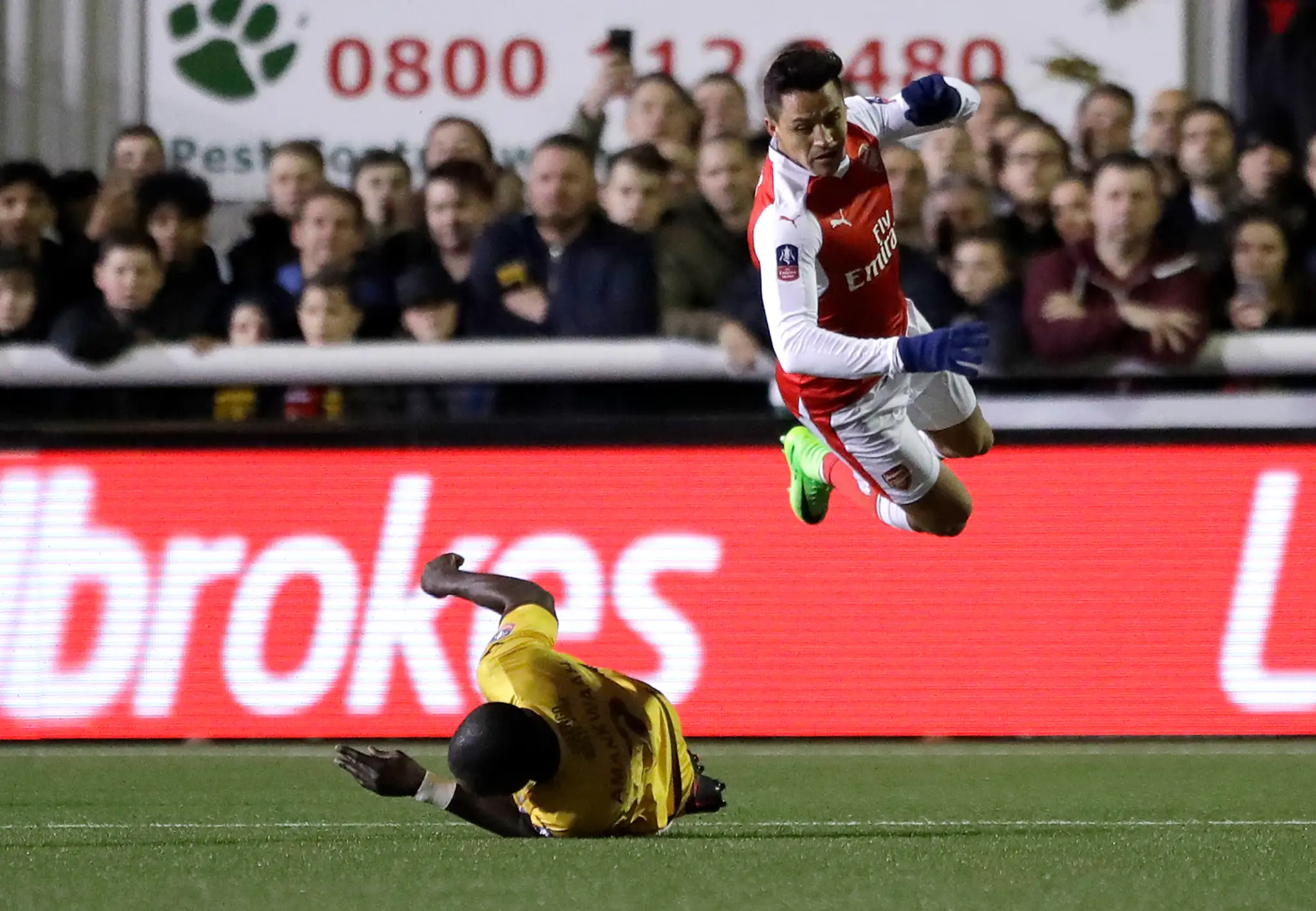 Hráč Arsenalu Alexis Sánchez vo výskoku po zákroku hráča Suttonu Kevina Amankwaaha v zápase FA Cupu.