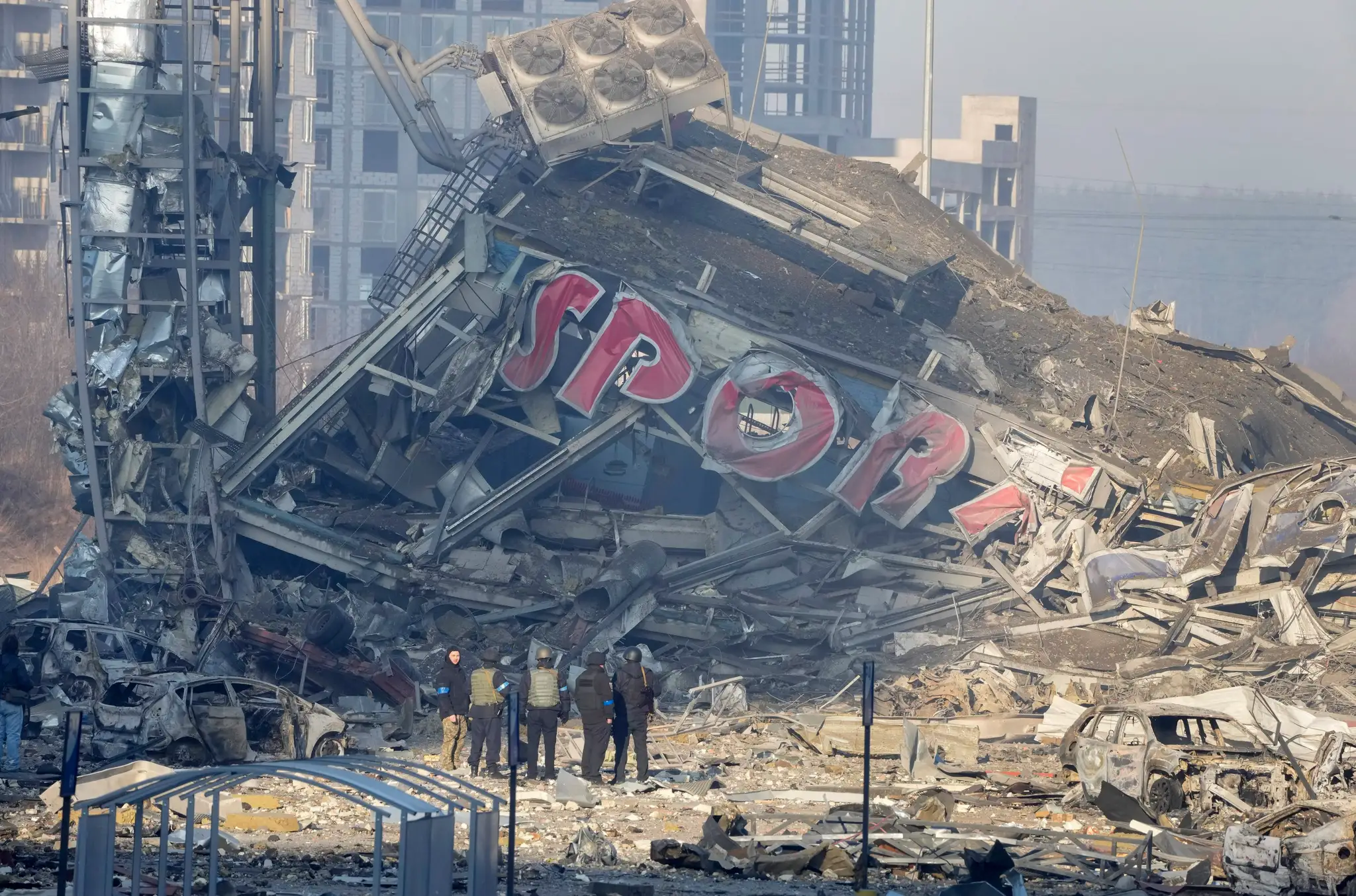 Ľudia vyšetrujú škody zničeného obchodného centra po ruskom bomardovaní v Kyjeve.