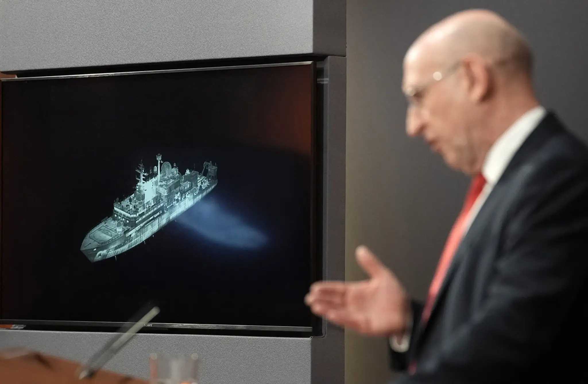 Britský minister obrany John Healey na pozadí obrazovky, na ktorej je zobrazená ruská vojenská loď Jantar pôsobiaca pri severnom pobreží Škótska.