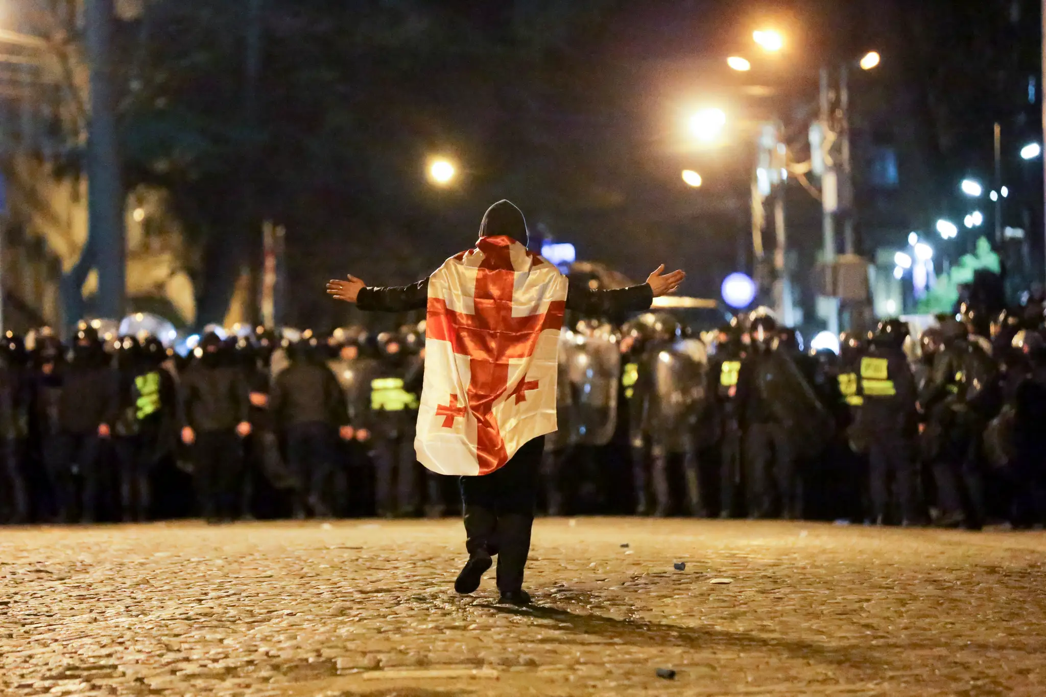 Demonštrant s gruzínskou vlajkou kráča k policajtom počas protestu pred budovou parlamentu v Tbilisi.