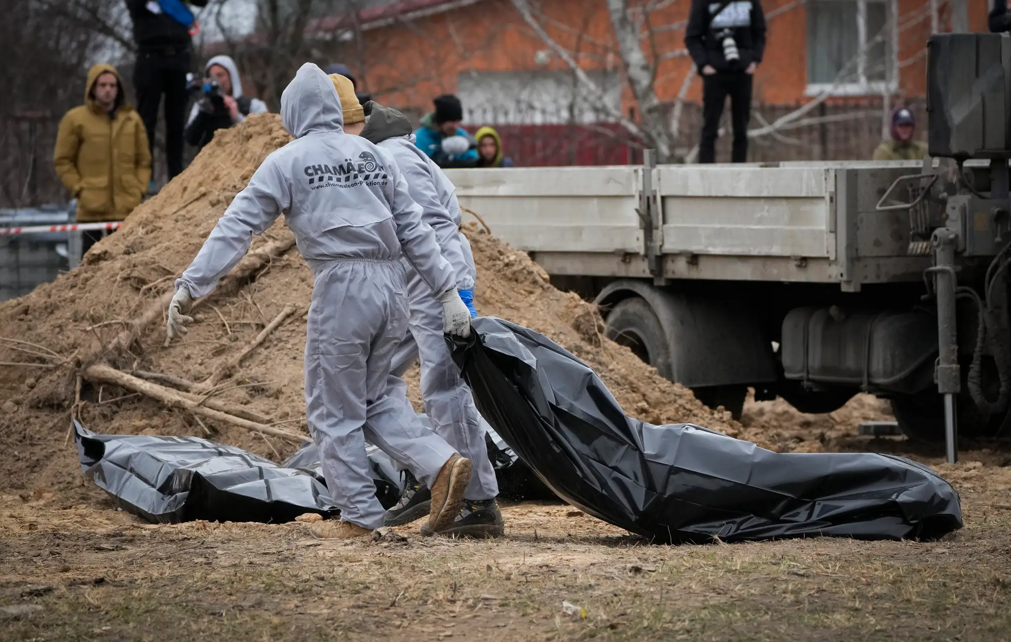 Muži v ochranných odevoch exhumujú telá civilistov v ukrajinskom meste Buča.
