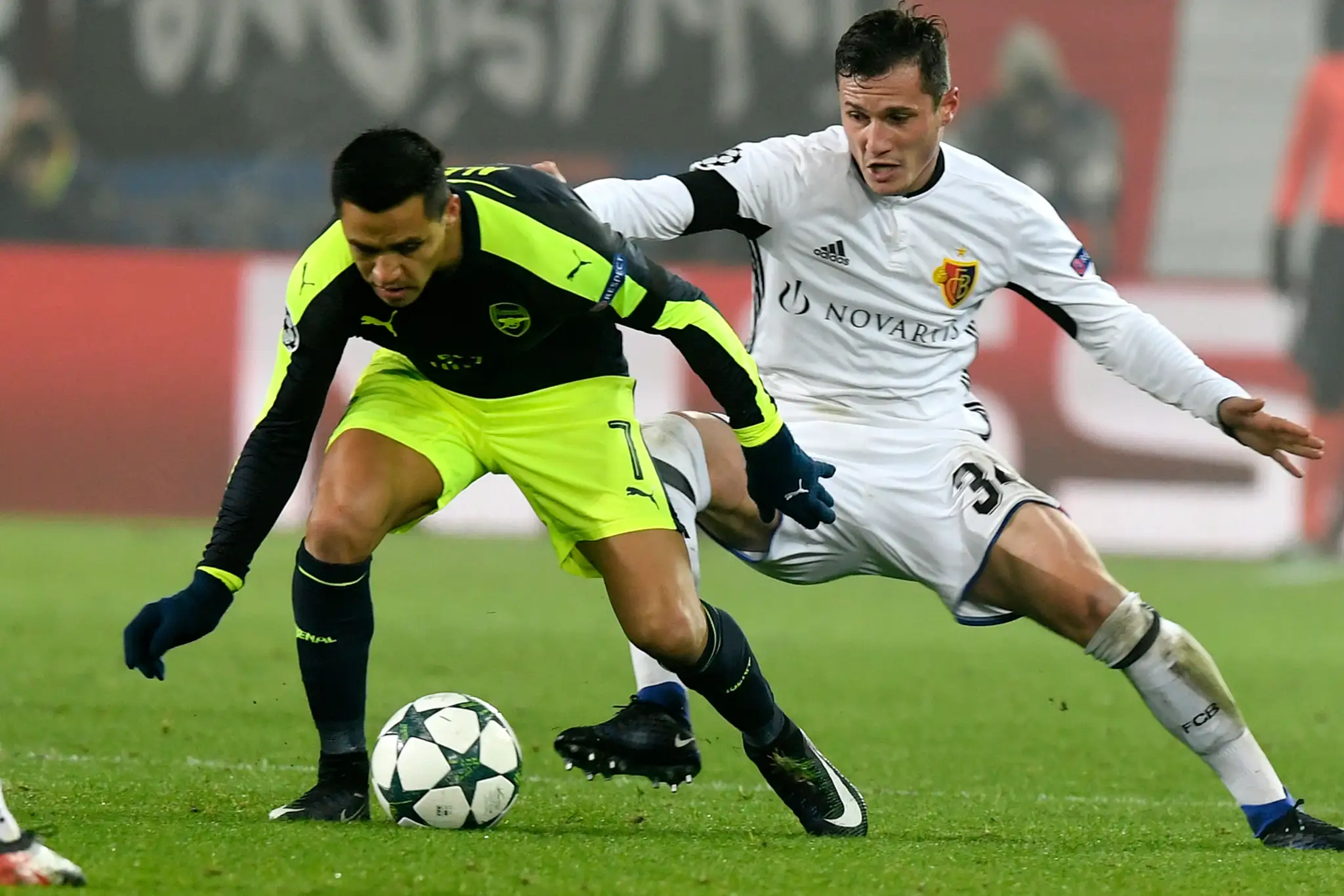 V súboji o loptu Taulant Xhaka (vzadu) z FC Bazilej proti Alexisovi Sánchezovi z Arsenalu v dueli LM.