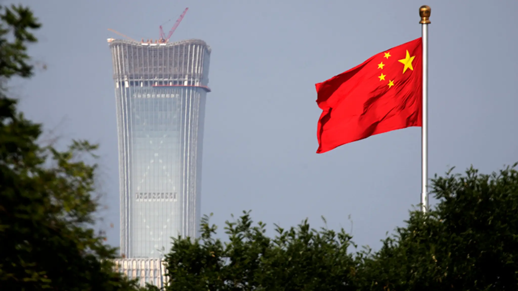 Čínska národná vlajka veje vedľa rozostavaného mrakodrapu China Zun v Pekingu.