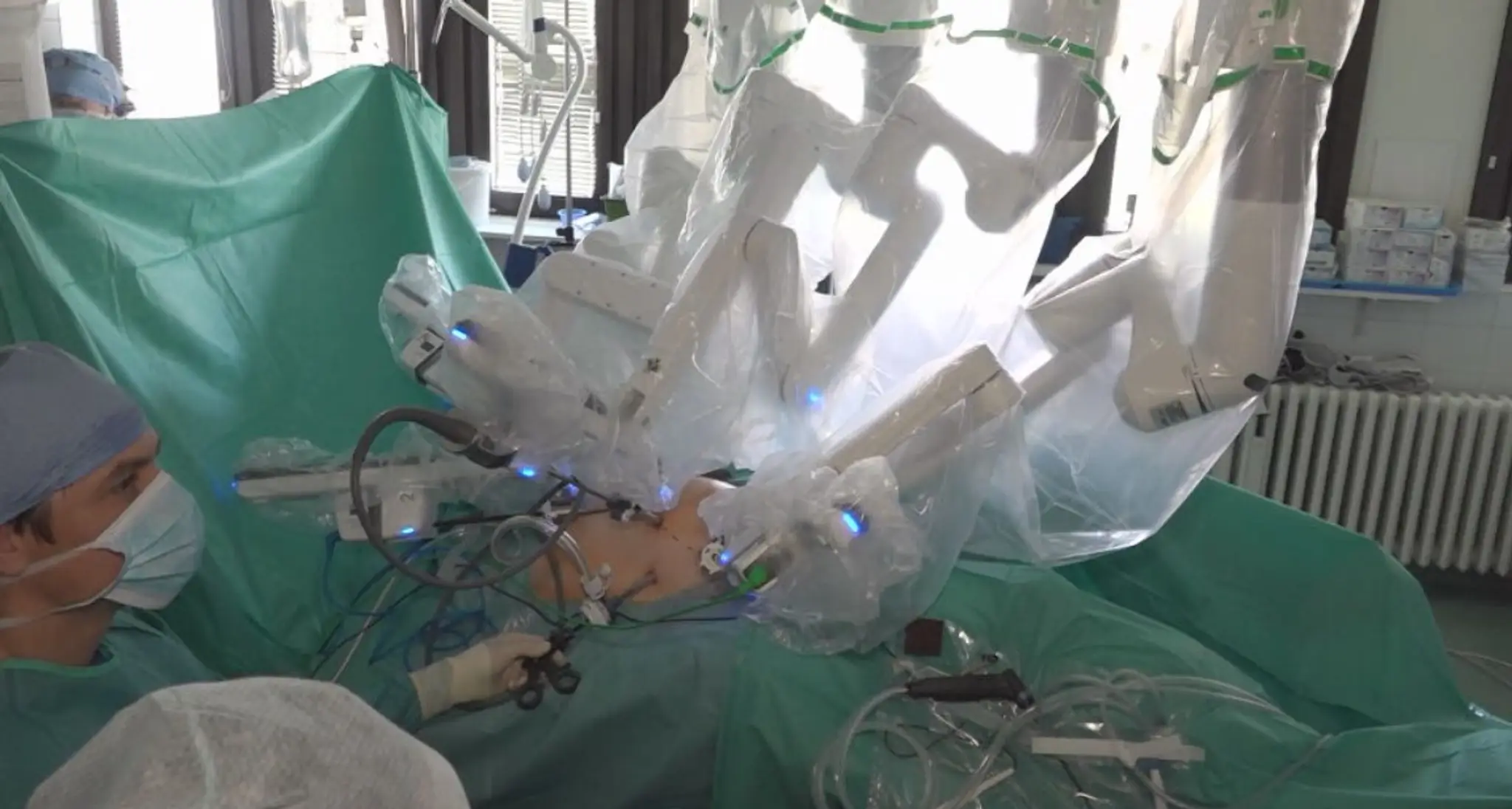 Na snímke prebieha operácia, ktorú vykonáva robot DaVinci. Na posteli leží pacient, ktorý má odhalené len brucho a v jeho okolí sú zdravotné sestry.