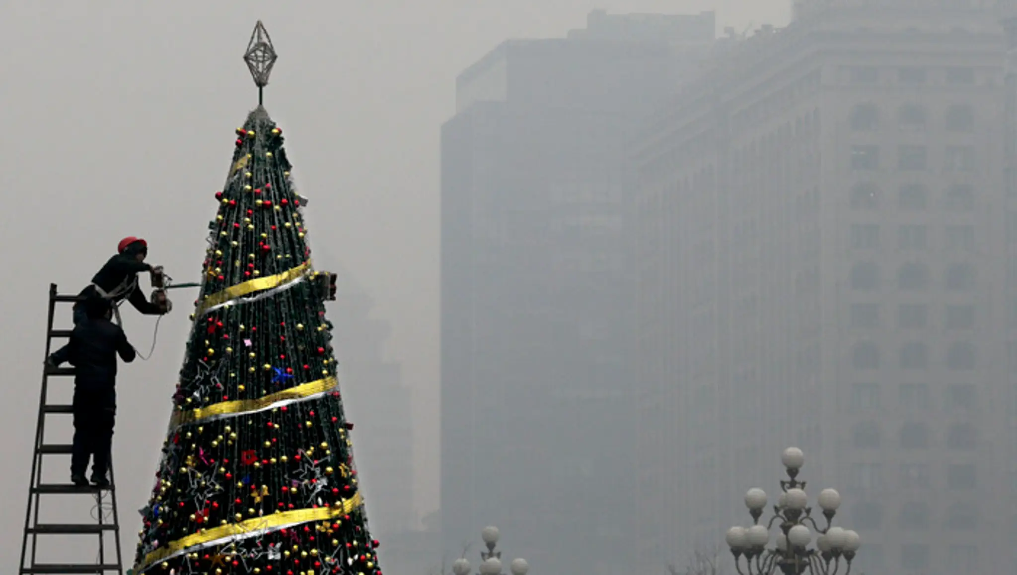 Zamestnanec zdobí vianočný stromček pred nákupným centrom počas smogovej pohotovosti v Pekingu.