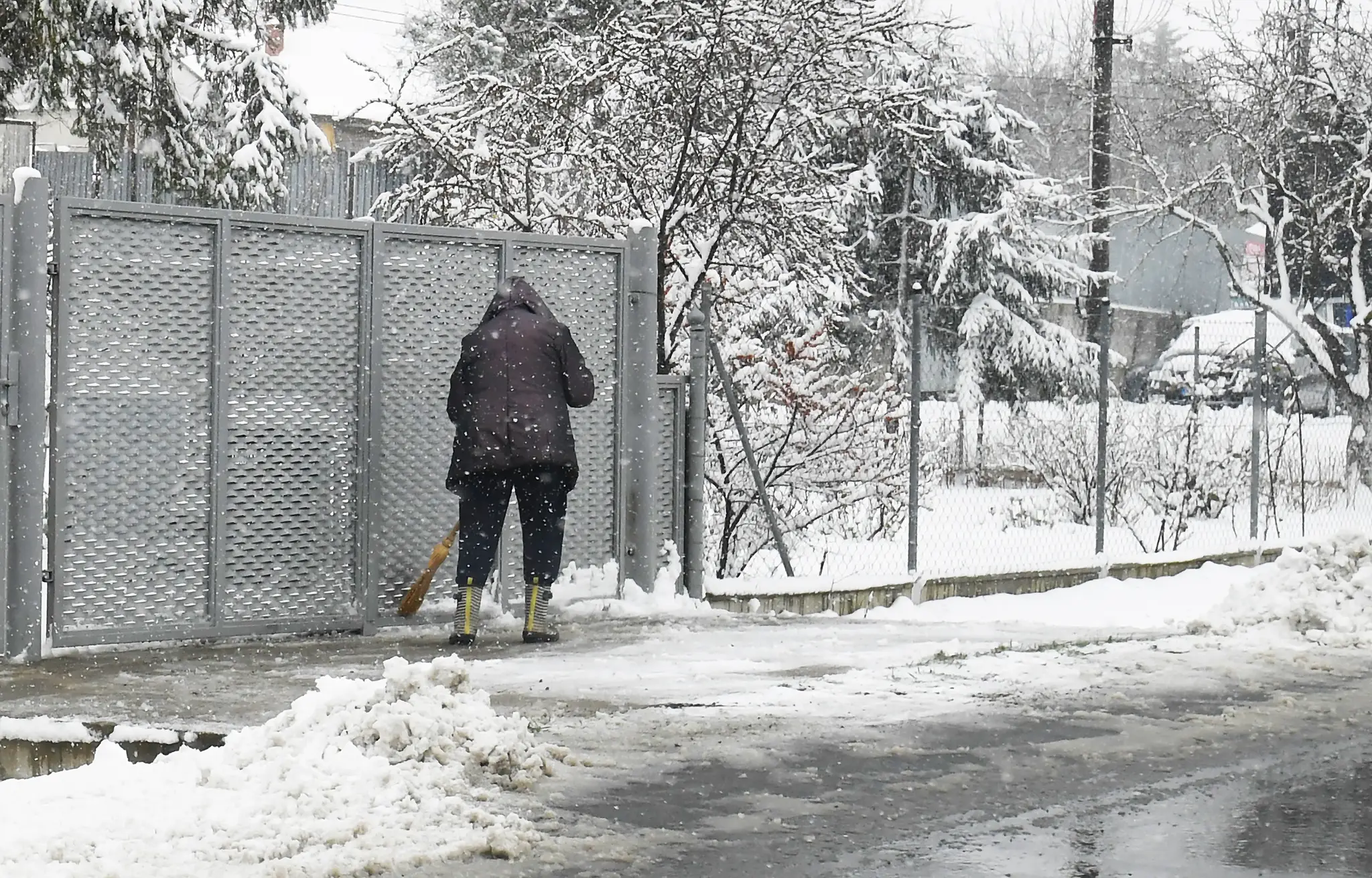 Žena odpratáva sneh z chodníka pred domom.