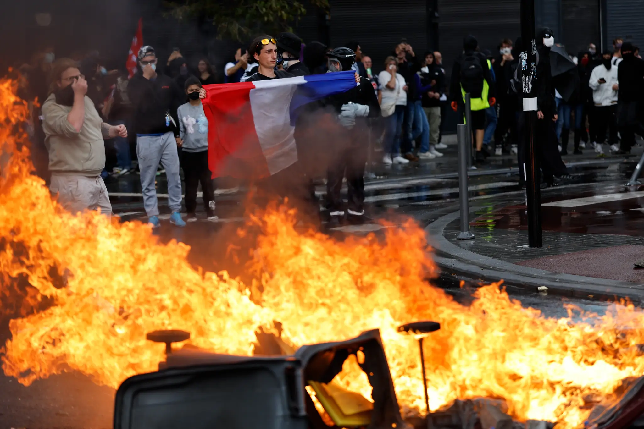 Demonštrant hnutia „Block Everything“ (Zablokujte všetko) drží francúzsku vlajku vedľa horiacich kontajnerov na odpadky v Lille.