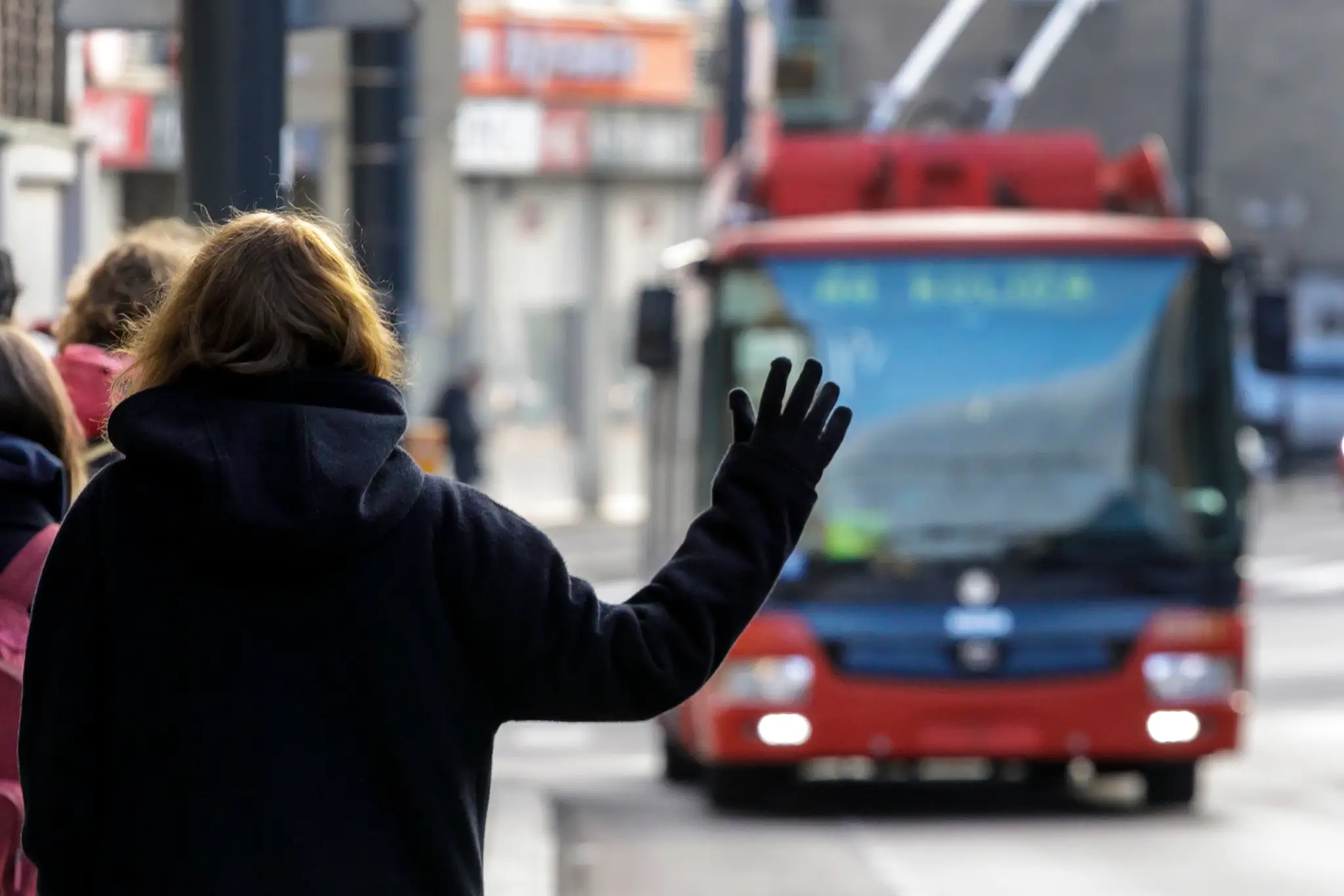Na snímke žena máva na zastávke na červený autobus MHD, ktorý sa k nej blíži.