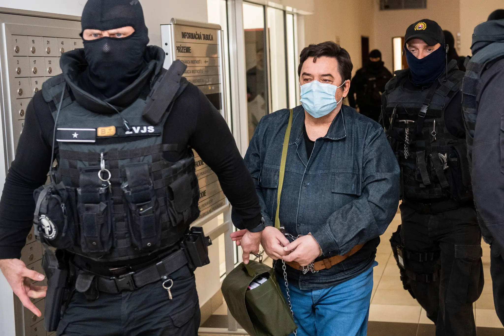 Na snímke je obvinený Marian Kočner na súde, sprevádza ho polícia a na tvári má modré rúško.
