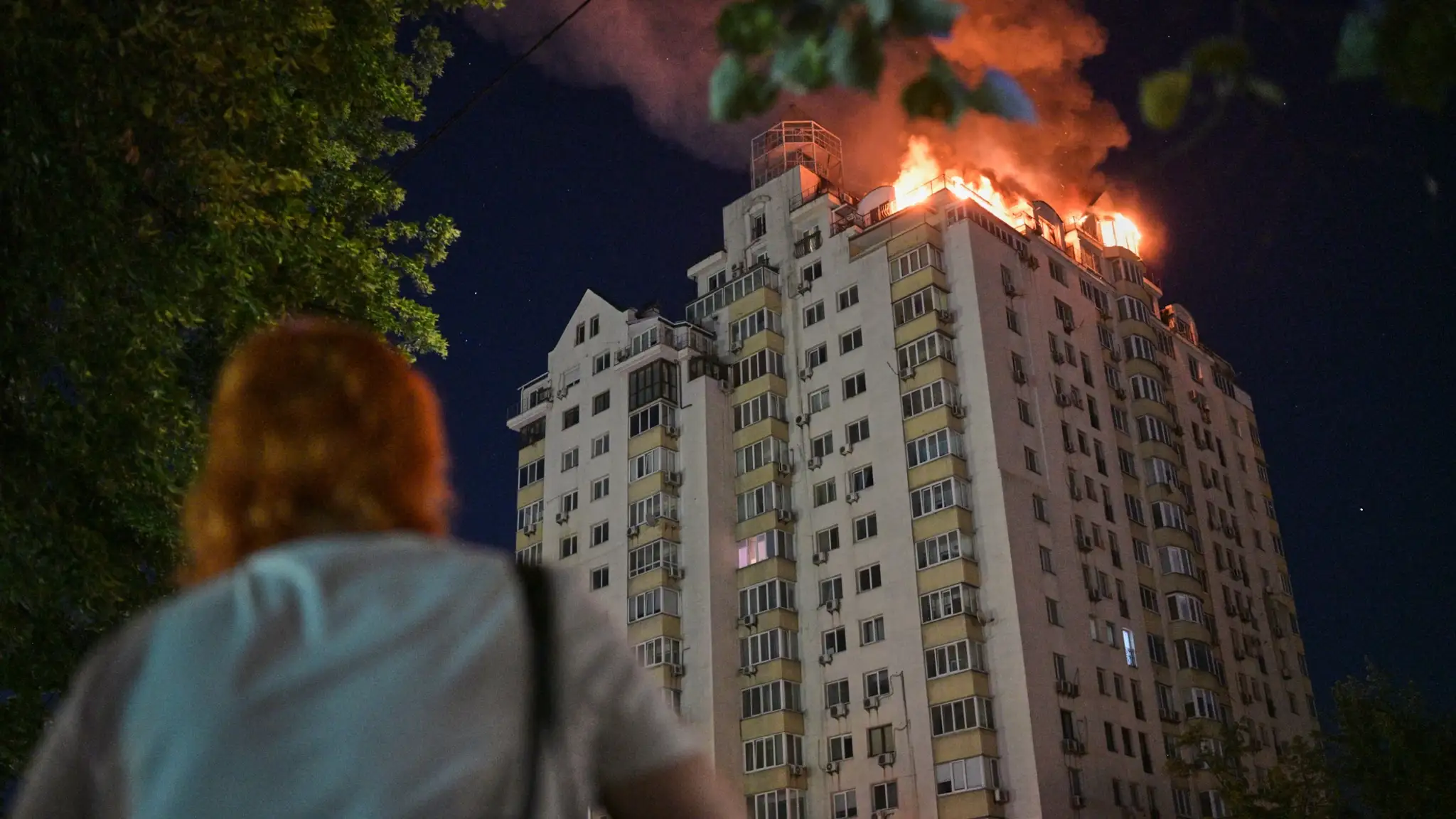 Žena sa pozerá na horiaci bytový dom po ruskom raketovom útoku v Kyjeve.