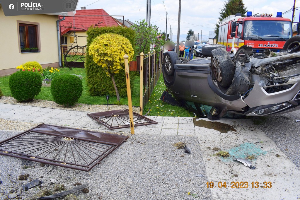 Na snímke je auto, ktoré skončilo po nehode prevrátené na streche. Vidieť je aj rozbitý plot a hasičské auto.