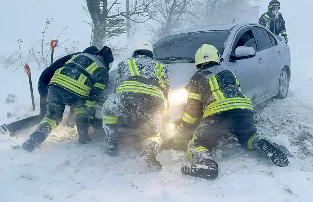 Ukrajinskí záchranári snažia odtlačiť auto, ktoré uviazlo na ceste počas snehovej víchrice v Odeskej oblasti.