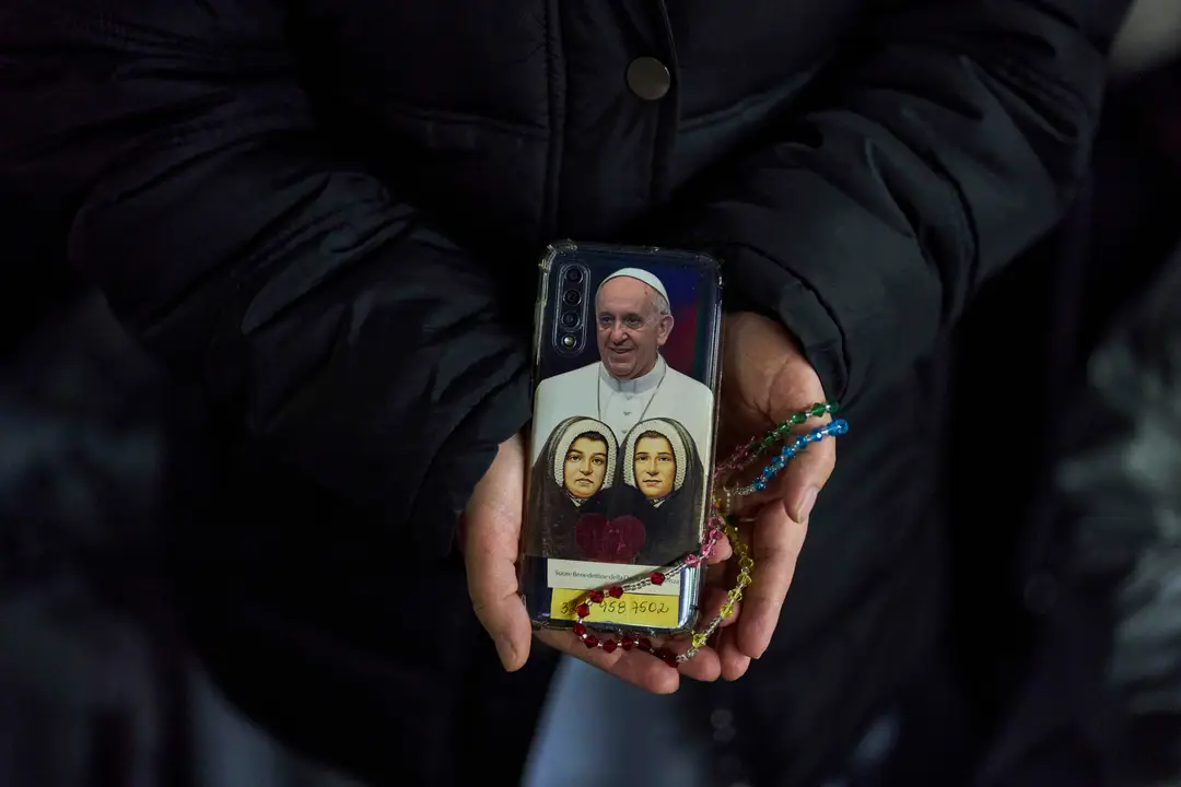 Mníška ukazuje zadný kryt svojho mobilného telefónu s fotografiou pápeža Františka počas večerného modlenia ruženca za jeho zdravie na Námestí sv. Petra.