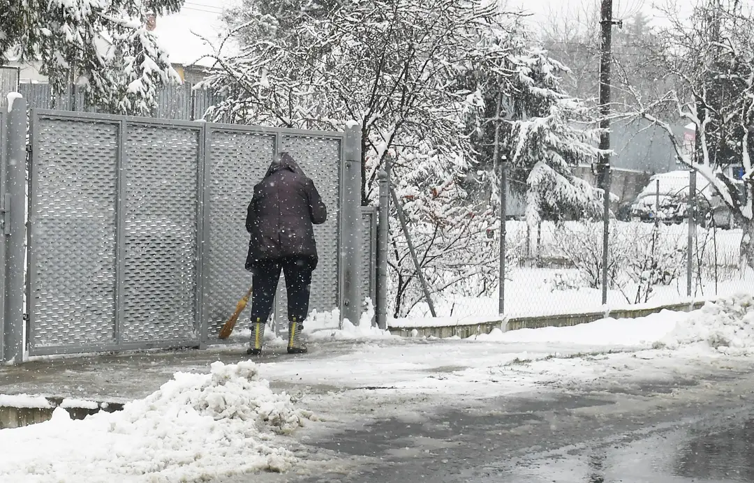 Žena odpratáva sneh z chodníka pred domom.