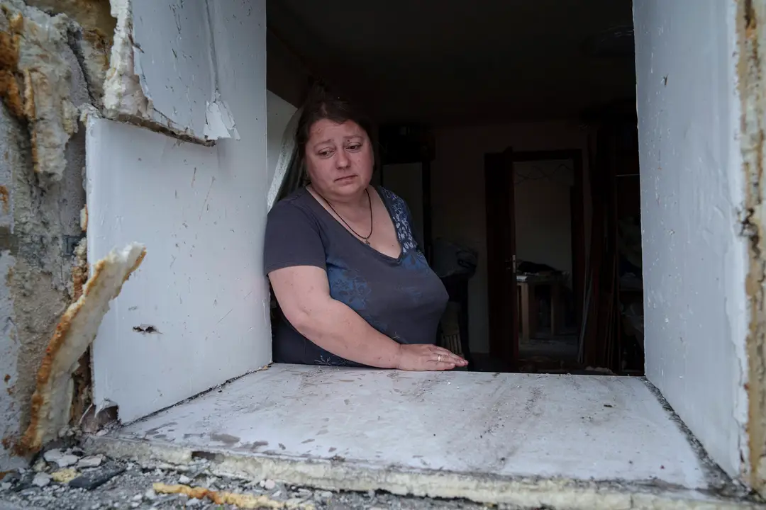 Žena sa pozerá cez okno svojho poškodeného domu po ruskom nálete na obytnú štvrť v Charkove.