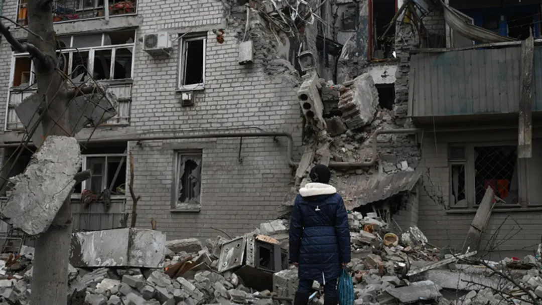 Žena sa pozerá na bytovku zničenú po nedávnom ruskom raketovom útoku v meste Časiv Jar v Doneckej oblasti.