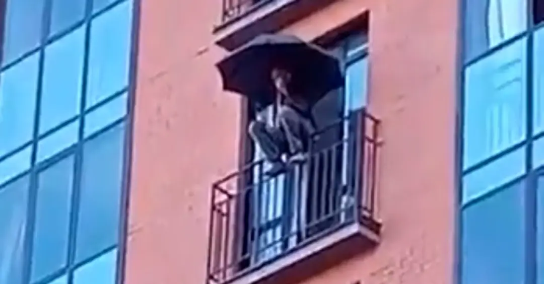 Muž s dáždnikom sedí na zábradlí krátko pred skokom.