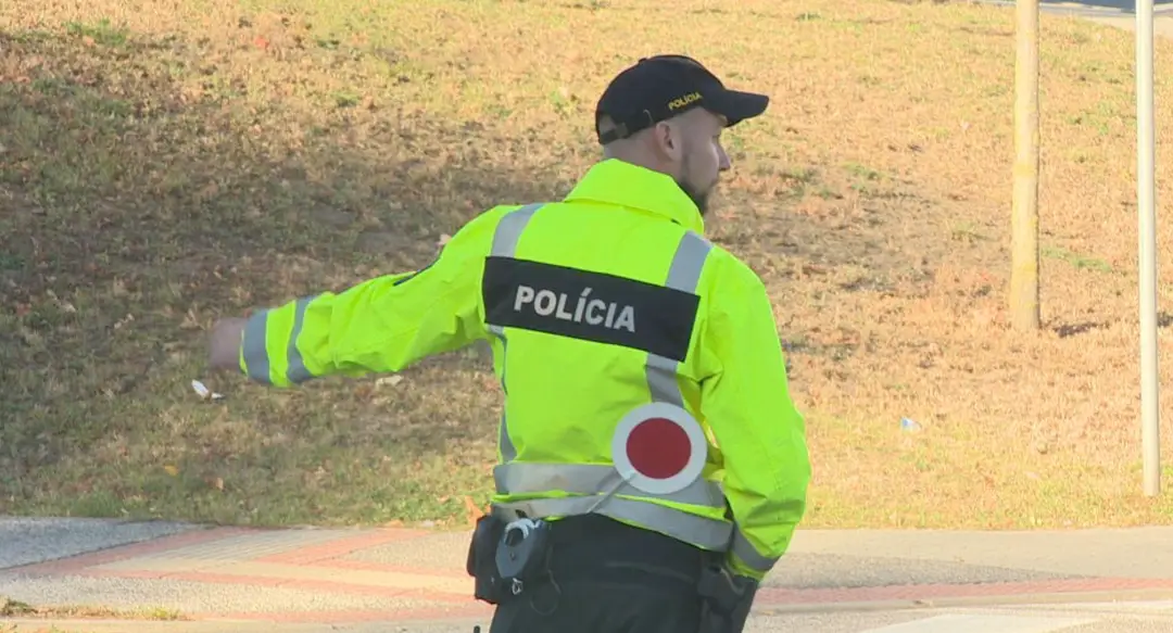 Na snímke je policajt v zltej bunde, ktory riadi dopravu. 