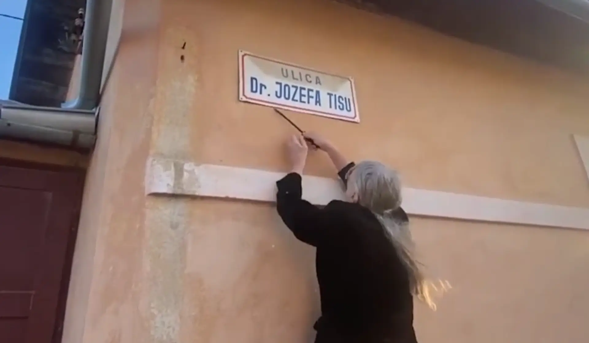 Na snímke občiansky aktivista strháva tabuľu ulice Jozefa Tisa vo Varíne.