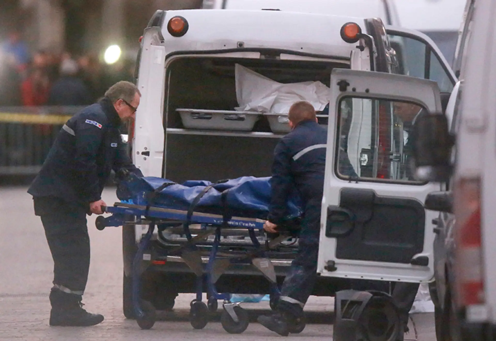 Dvaja muži odnášajú telo do pohrebného auta po policajnom zásahu proti skupine extrémistov v Saint-Denis.