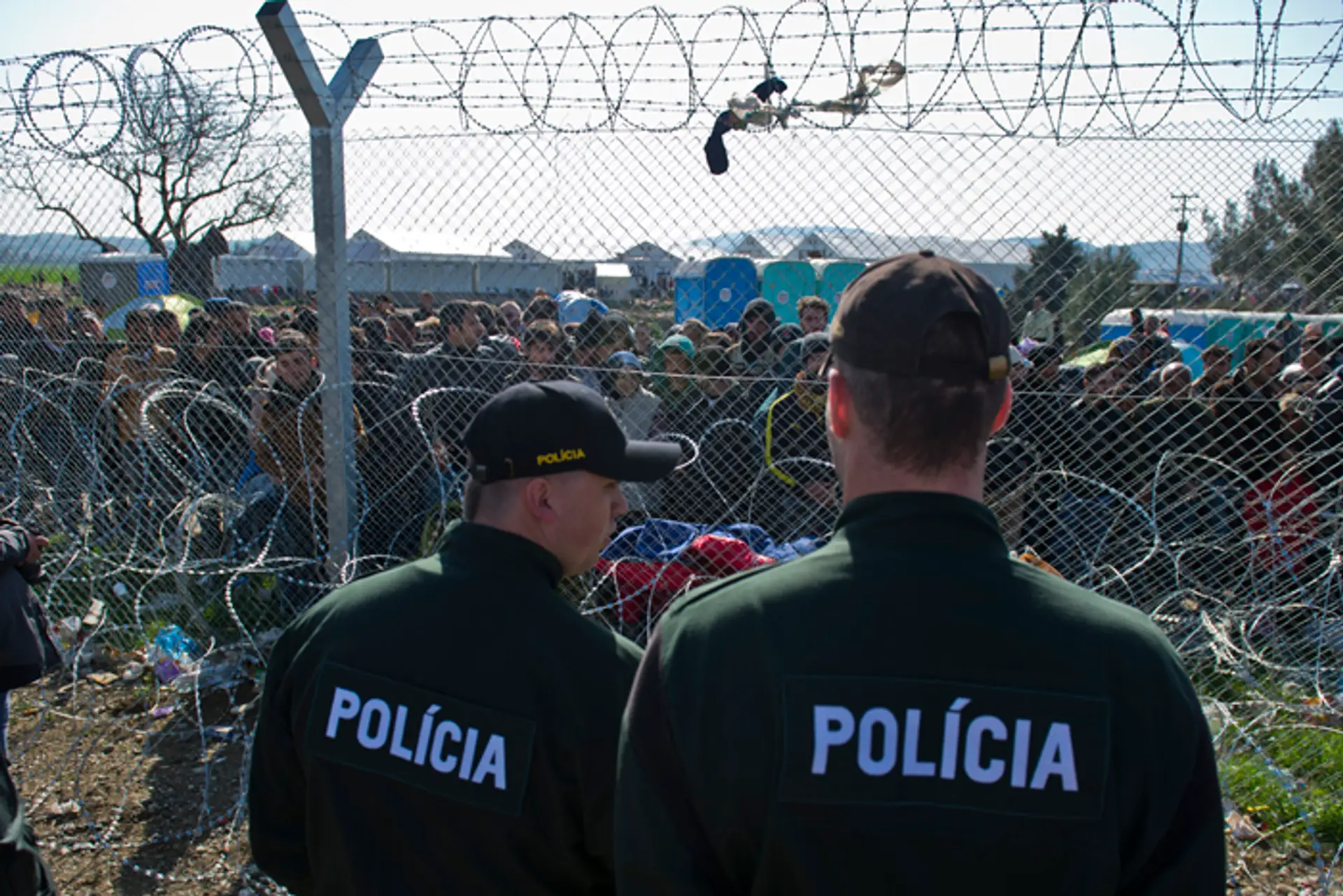 Na snímke migranti na gréckej strane hranice a slovenskí policajti. 
