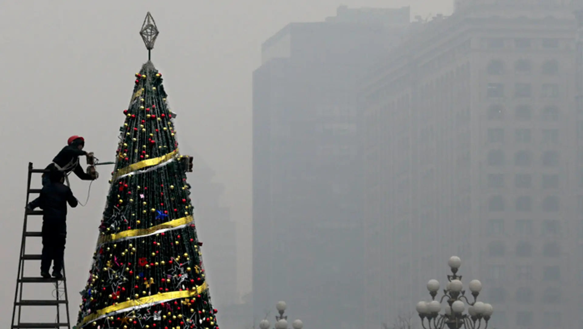 Zamestnanec zdobí vianočný stromček pred nákupným centrom počas smogovej pohotovosti v Pekingu.