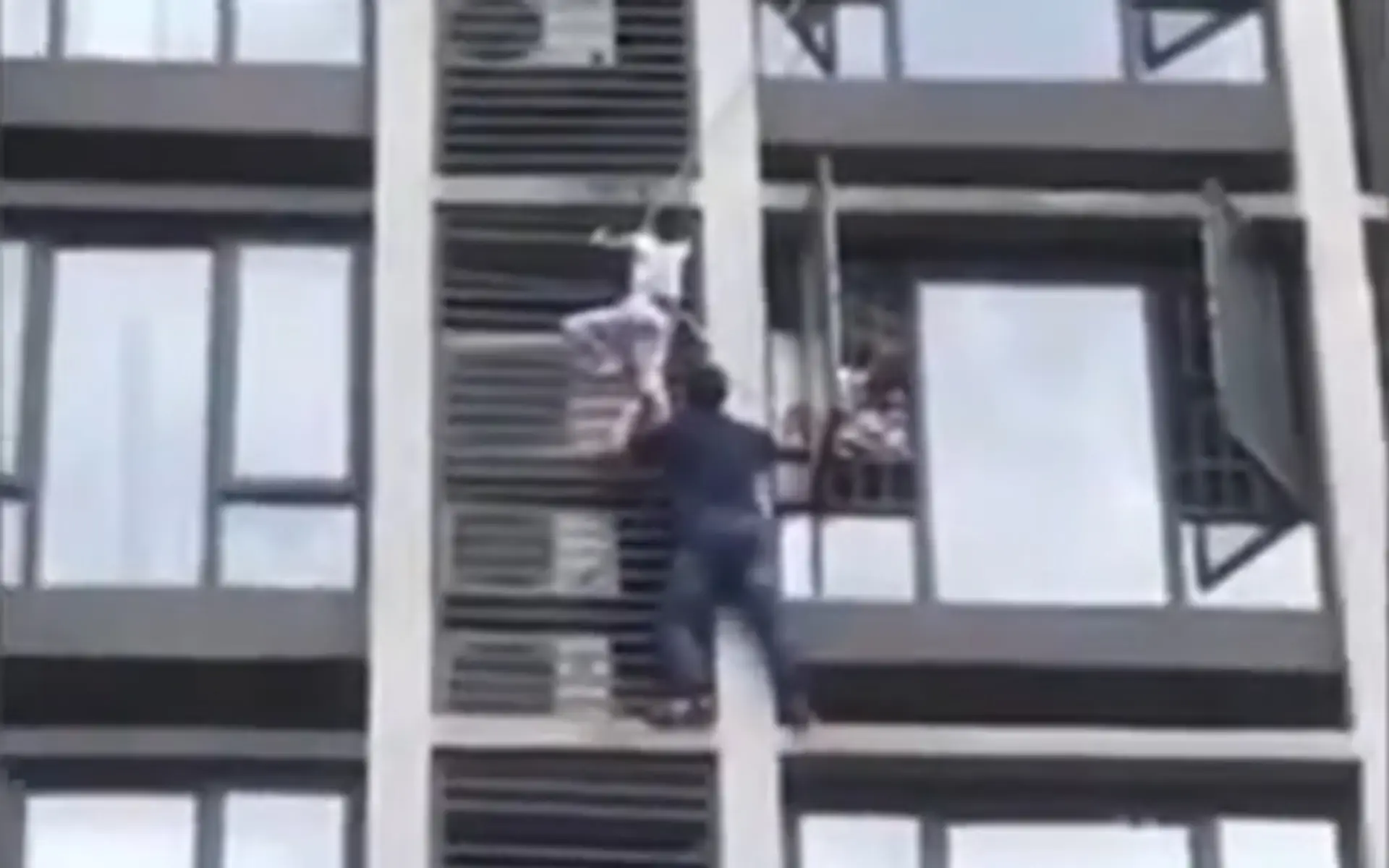 Otec zachraňuje syna visiaceho z klimatizácie na priečelí budovy.