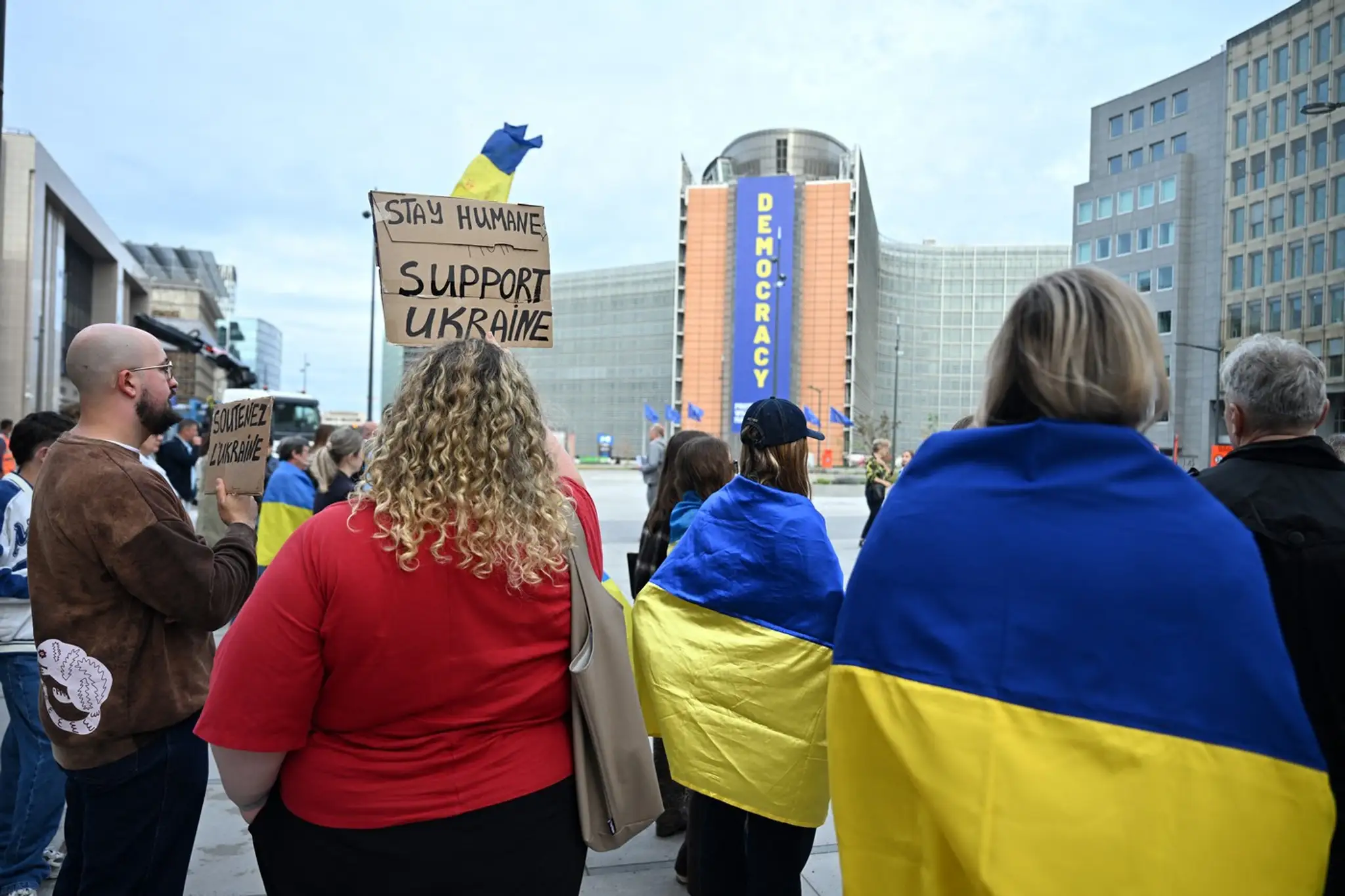 Ukrajinci sa zhromažďujú s ukrajinskými vlajkami a kuframi pred budovou Rady Európskej únie.