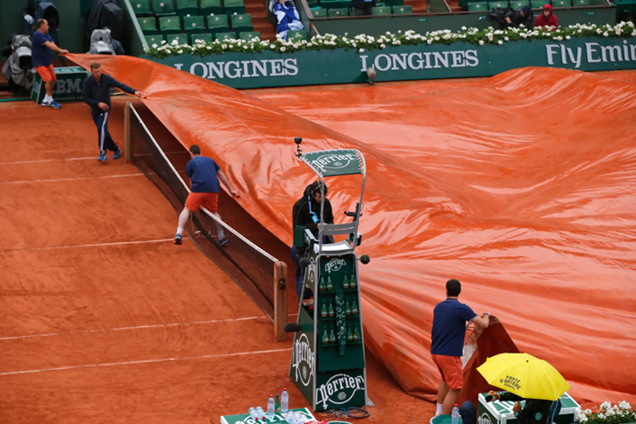 Pracovníci na Roland Garros zakrývajú antukový povrch pred dažďom.