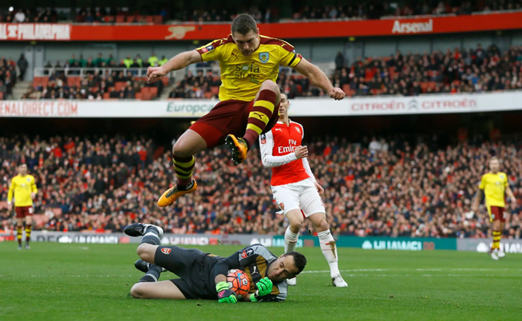 Hráč Sam Vokes (Burnley) skáče ponad brankára Davida Ospinu (Arsenal).