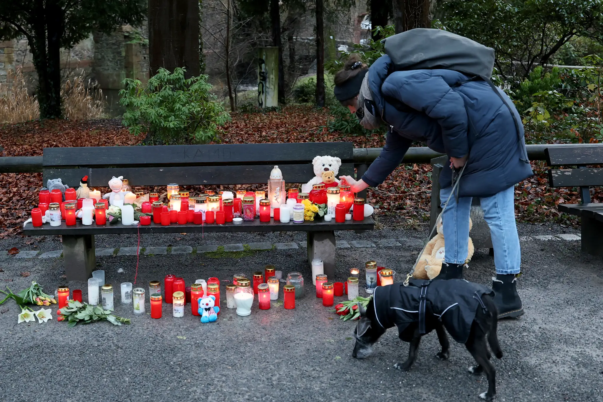 Žena kladie sviečku na lavičku vedľa kvetov a plyšových hračiek po smrteľnom útoku v parku v nemeckom Aschaffenburgu.