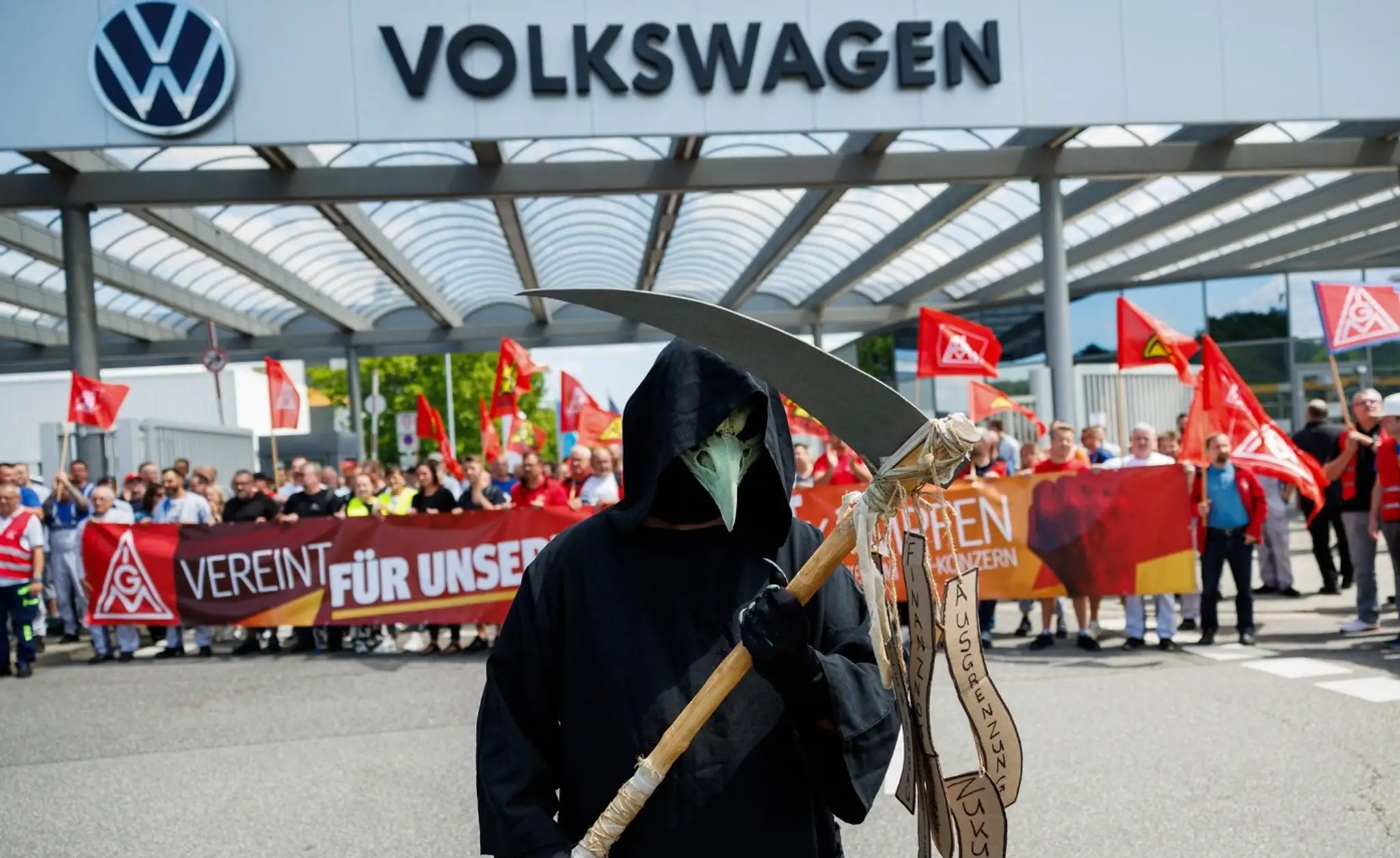 Účastník v kostýme Smrťky stojí pred vchodom do závodu, zatiaľ čo zamestnanci nemeckého výrobcu automobilov Volkswagen.