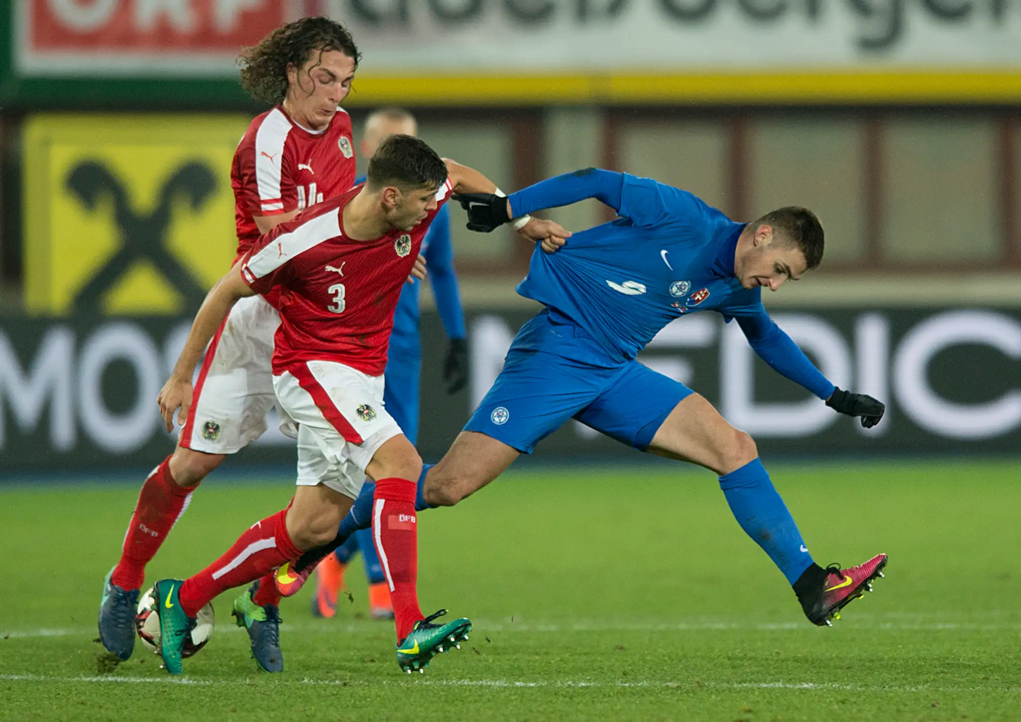 Matúš Bero (v modrom) proti dvojici rakúskych hráčov Aleksandarovi Dragovičovi (v strede) a kapitánovi Julianovi Baumgartlingeno