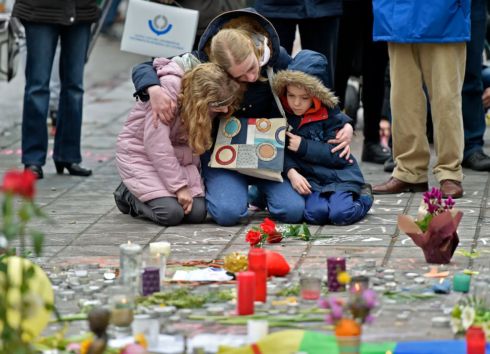 Žena s deťmí kľačí na pamiatku obetí  bombových útokov v Bruseli.