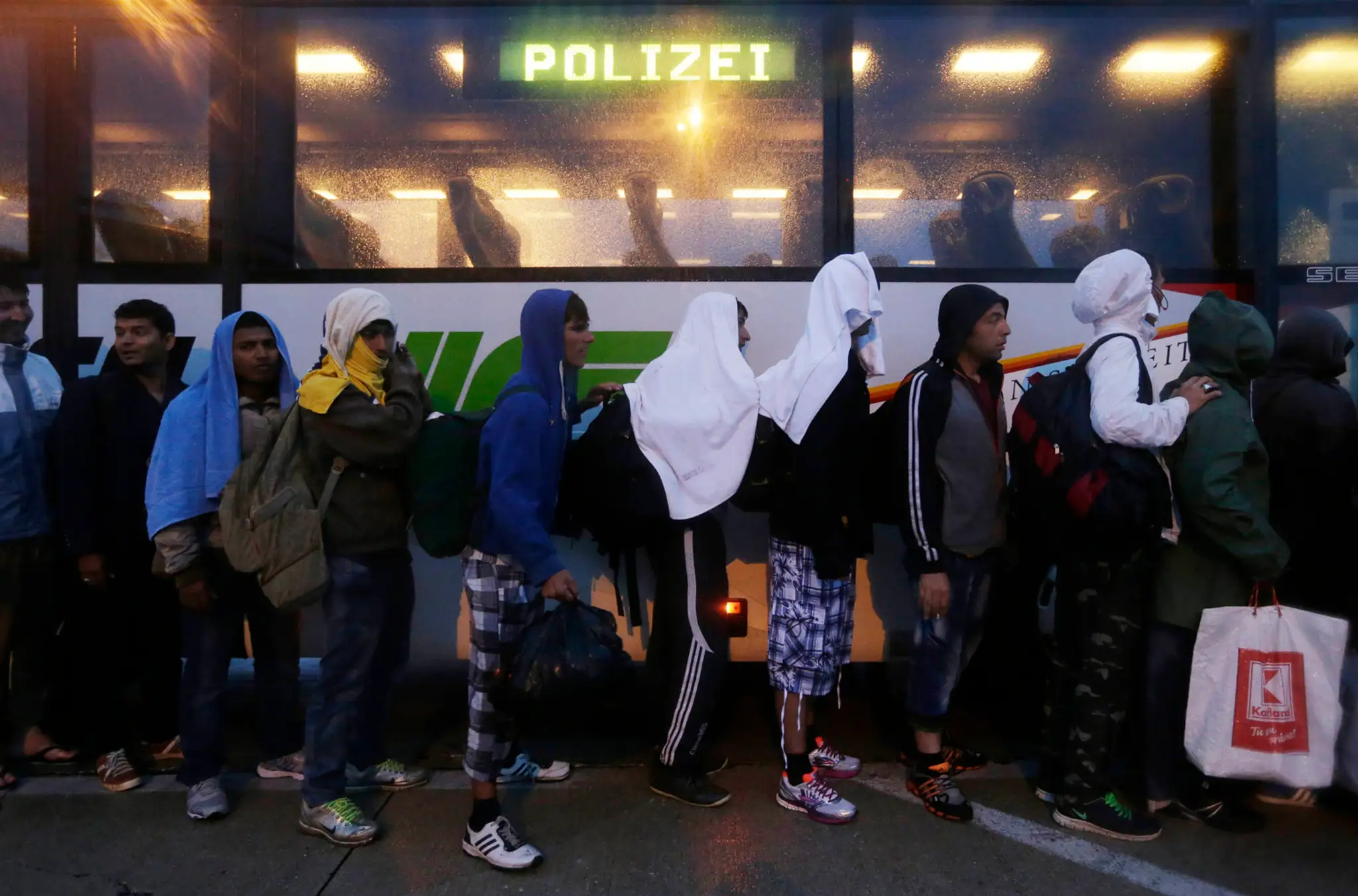Migranti v rade pred policajným autobusom na maďarsko-rakúskej hranici.