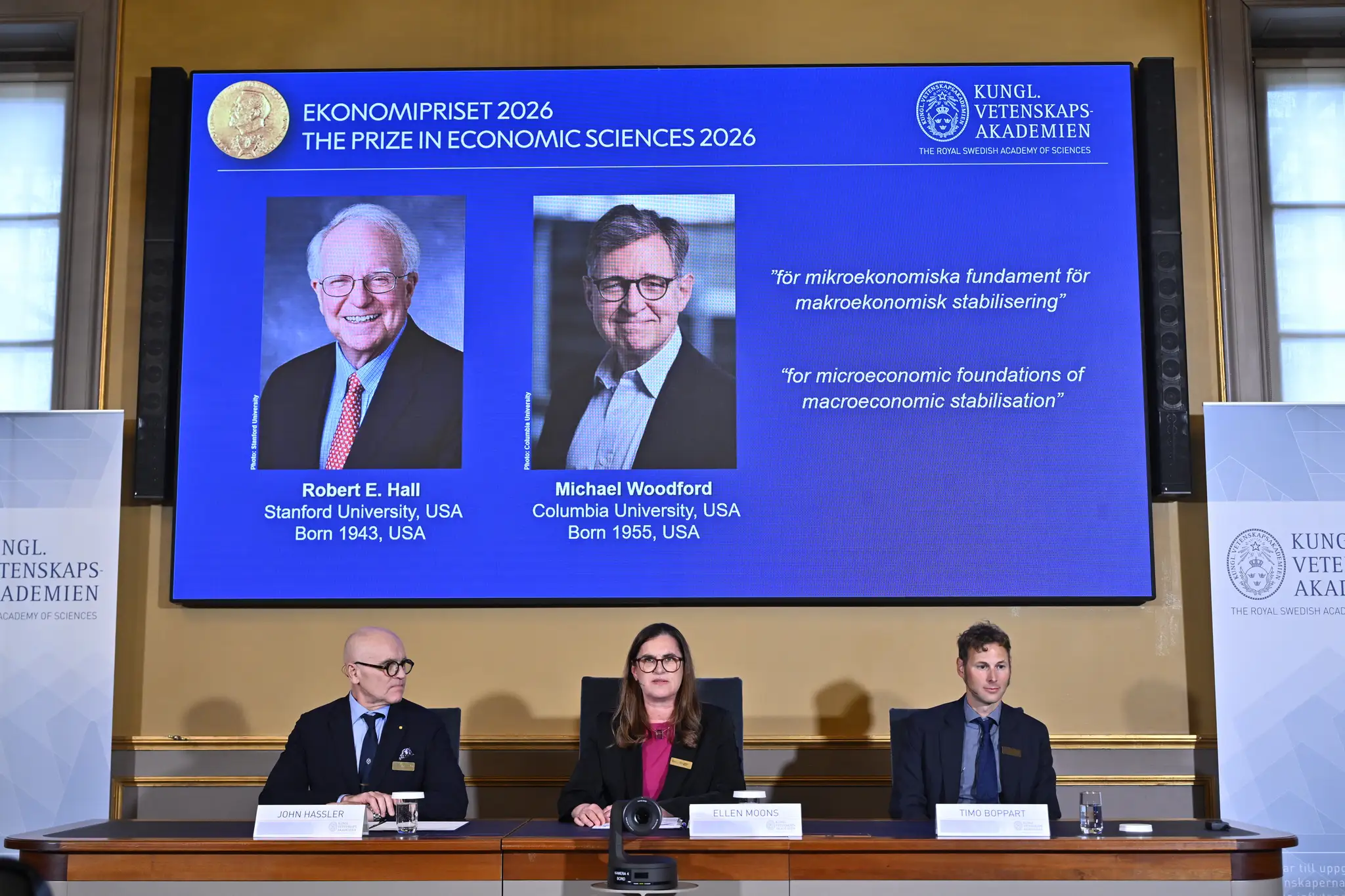 Na veľkoplošnej obrazovke sú americkí ekonómovia Robert E. Hall (vľavo) a Michael Woodford, ktorým udelili Nobelovu cenu za ekonómiu za rok 2026.