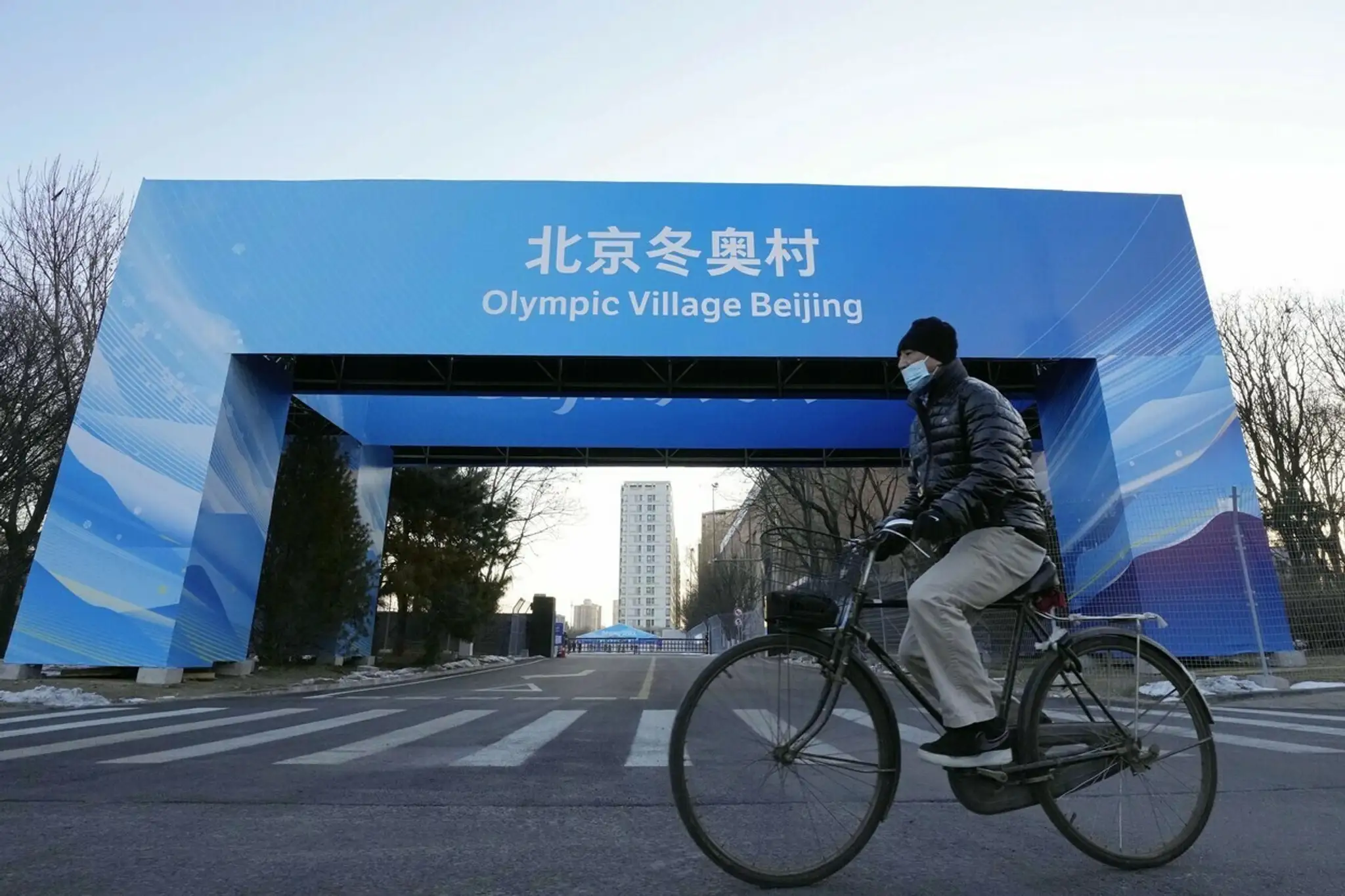 Muž prechádza na bicykli okolo brány do olympijskej dediny.