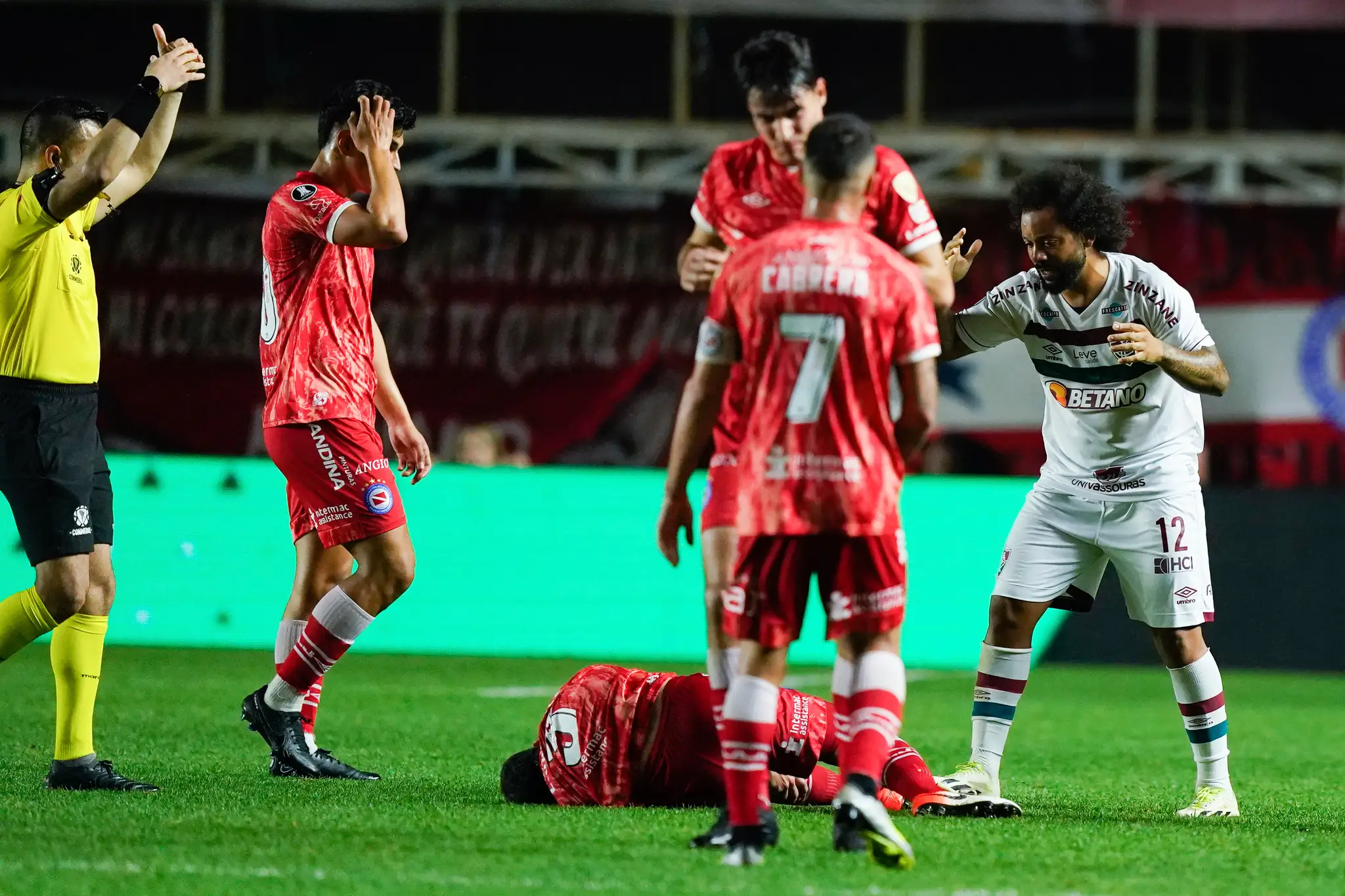 Futbalista Luciano Sanchez  z tímu Argentinos Juniors leží na zemi po faule obrancu Marcela (vpravo) z Fluminense.